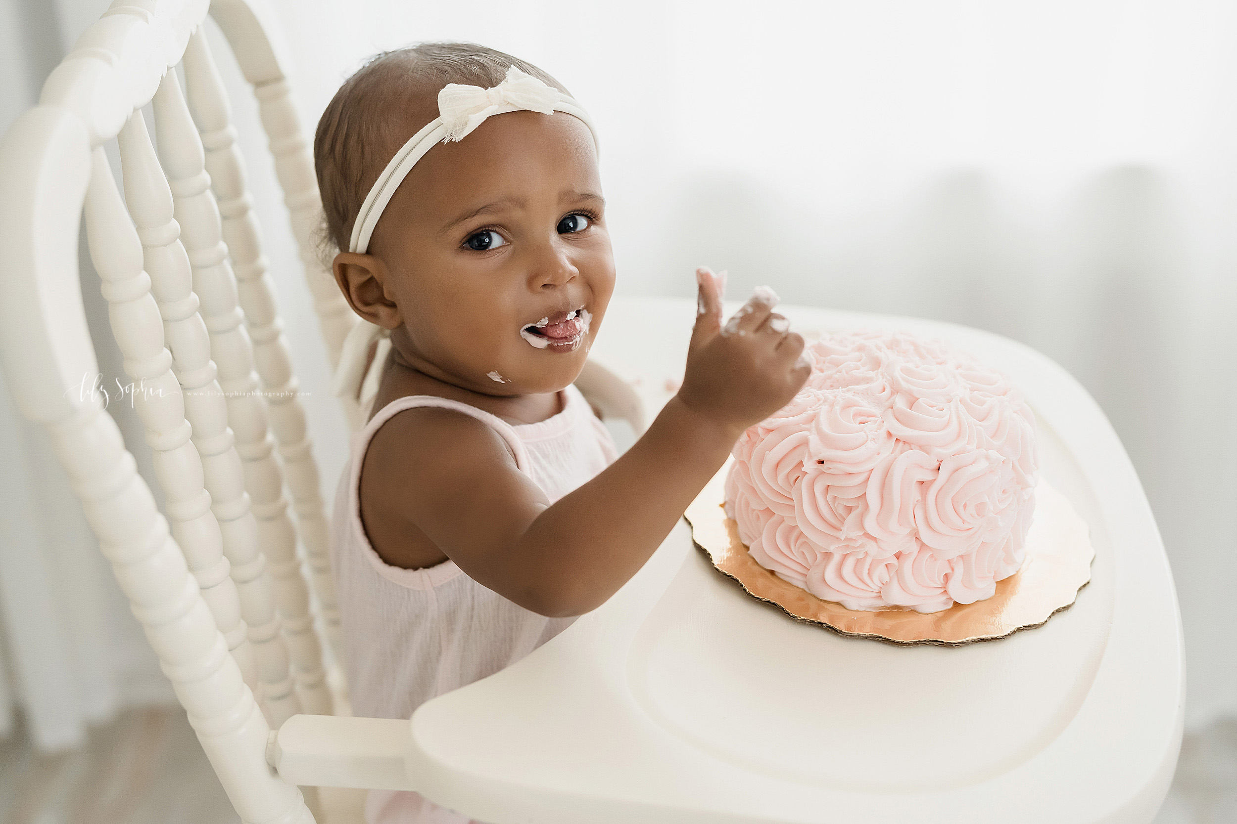 Photo of a one year old African-American baby girl giving a thumbs up for her birthday cake as she enjoys the frosting while sitting in an Atlanta studio in an antique highchair. 
