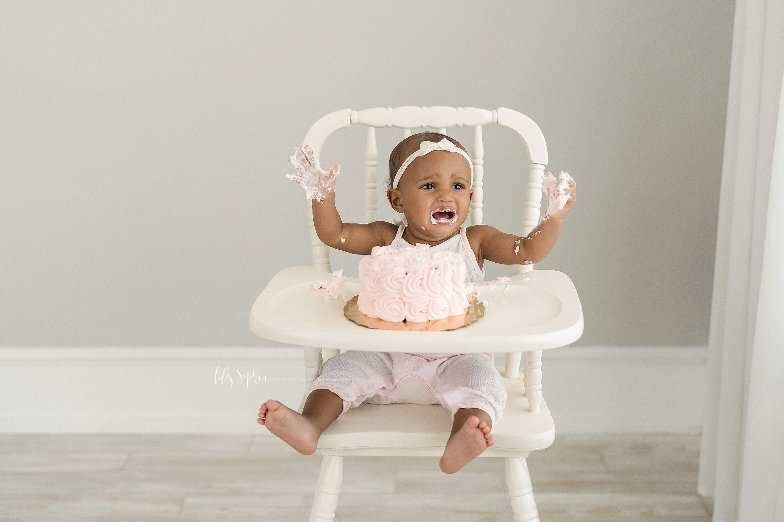  Milestone photo of an African-American baby girl as she sits in an antique highchair in Atlanta and cries because her hands are covered with icing. 