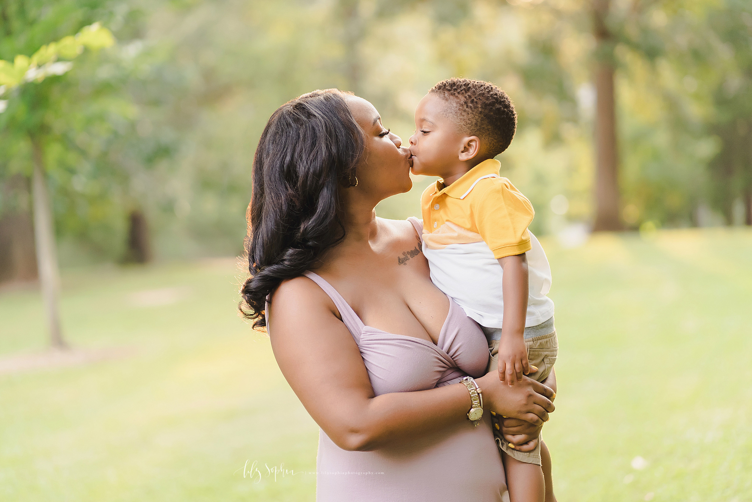  Family photo of an African-American mother and her three year old son as she holds him in her arms and the two of them kiss as the sun sets in an Atlanta park. 