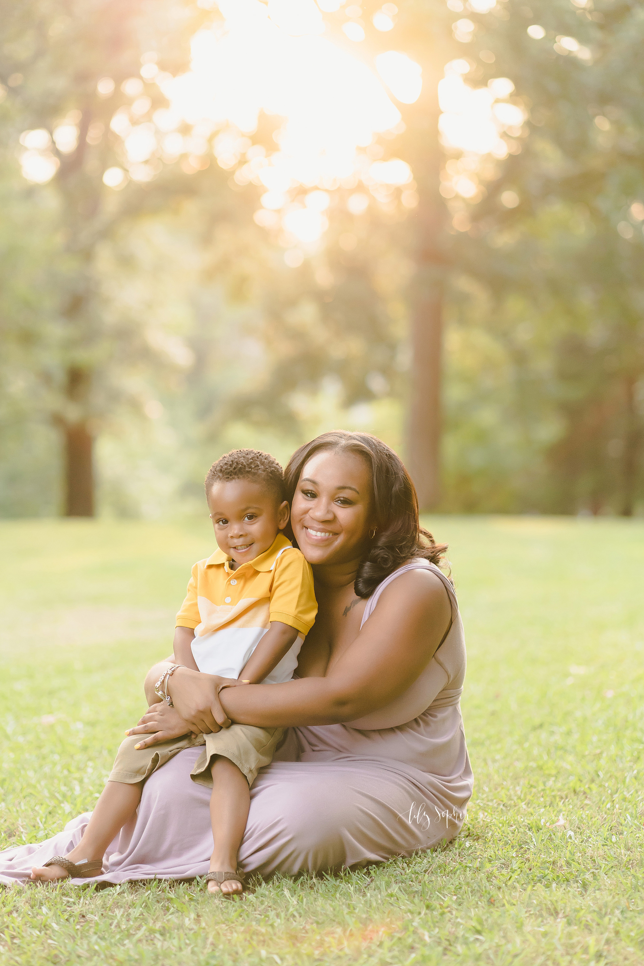  Family photo of an African-American mother holding her son on her lap as she sits on the grass in an Atlanta park at sunset. 