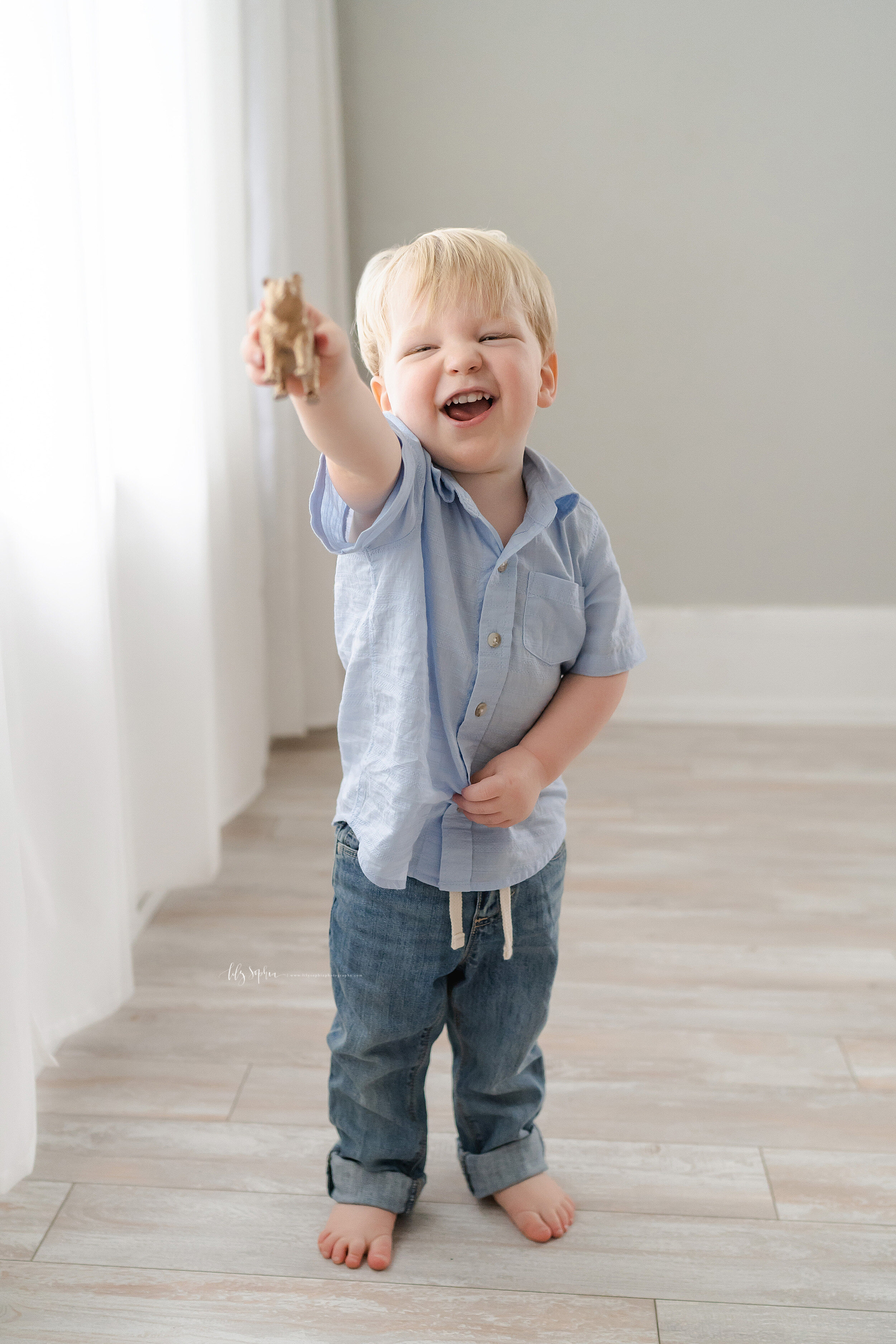 Photo of a two year old blond haired boy as he growls like a bear and reaches out his left hand to show his wooden bear in a Poncey Highlands natural light studio. 