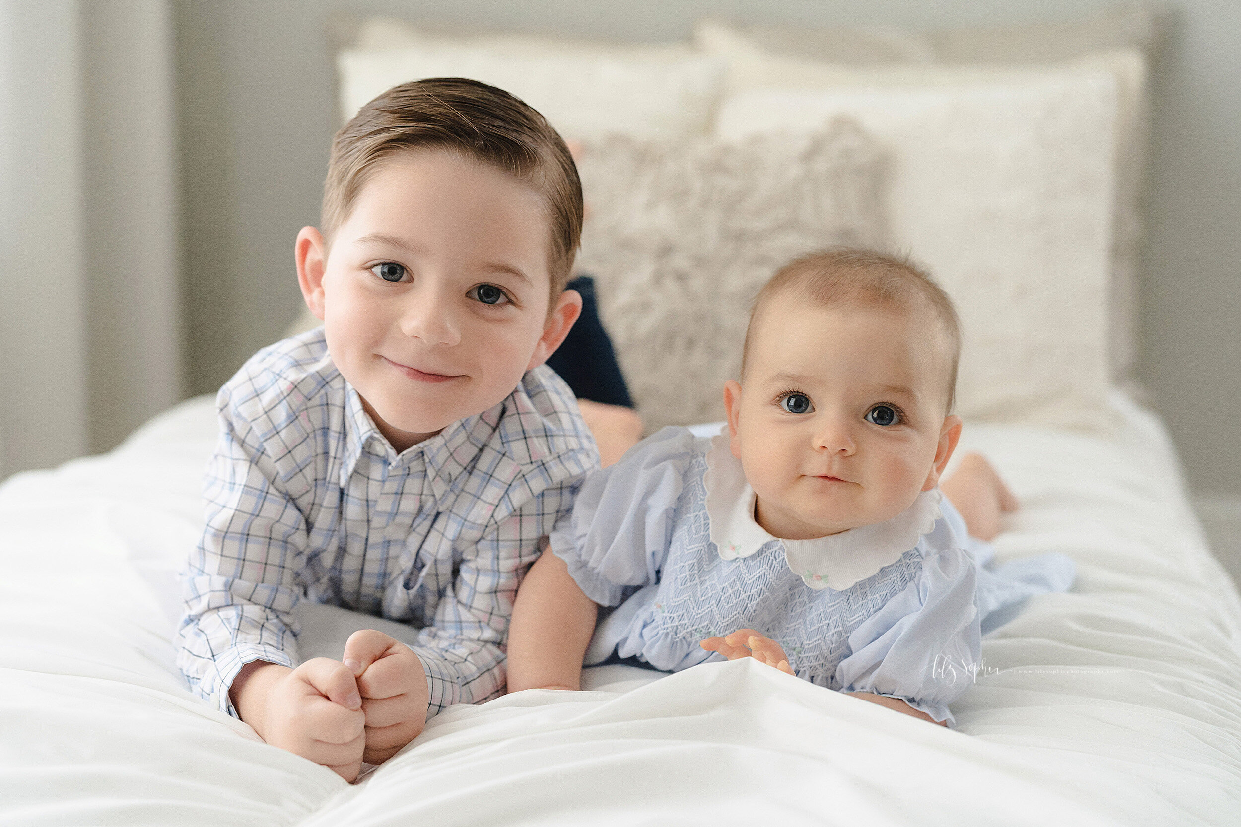  Family photo of a brother and his nine month old baby sister as they lie on their stomachs next to one another on a bed in a natural light studio near the Buckhead area of Atlanta. 