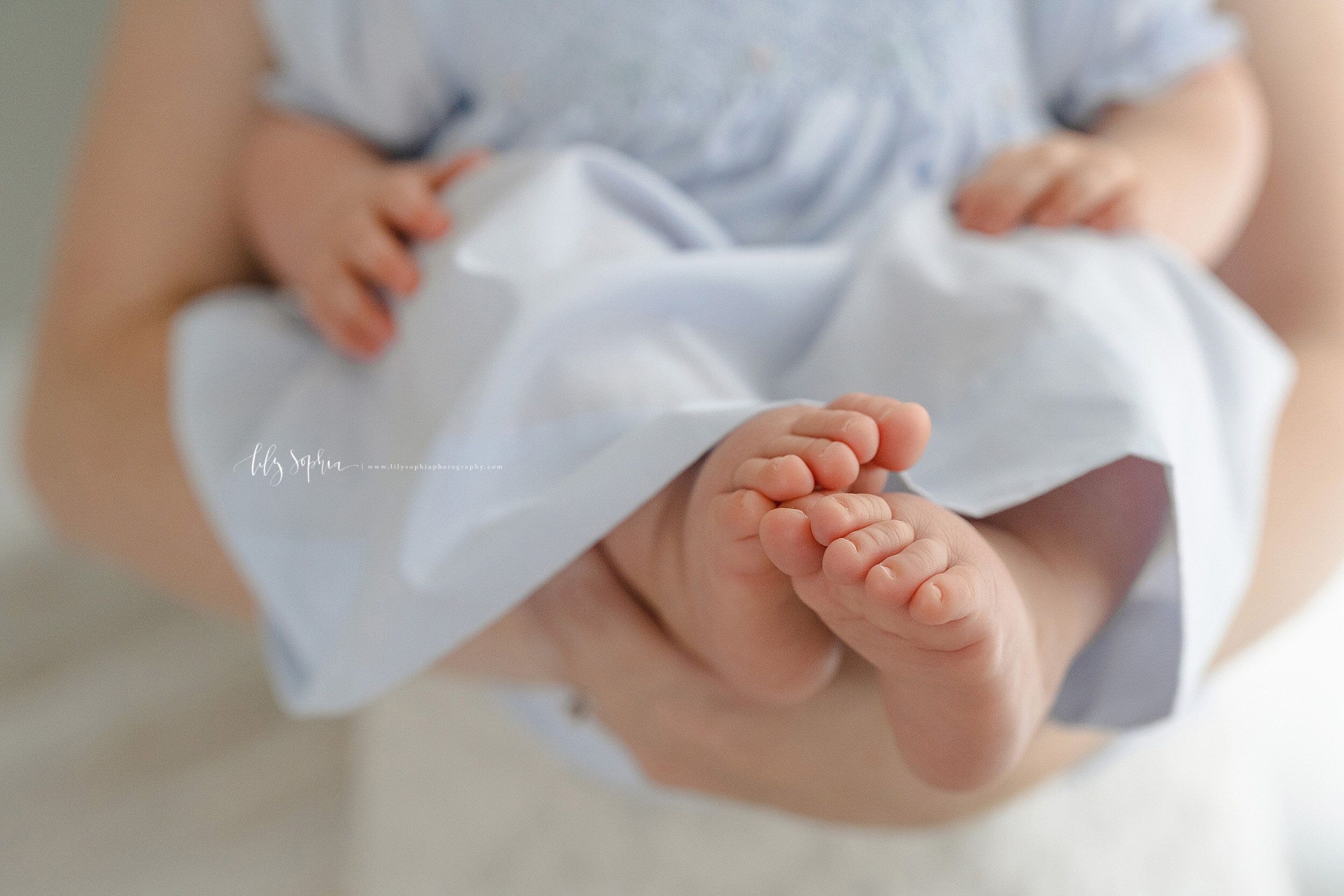  Close-up photo of the toes and feet of a nine month old baby girl as she is held by her mom taken in a studio in the Poncey-Highland area of Atlanta in natural light. 