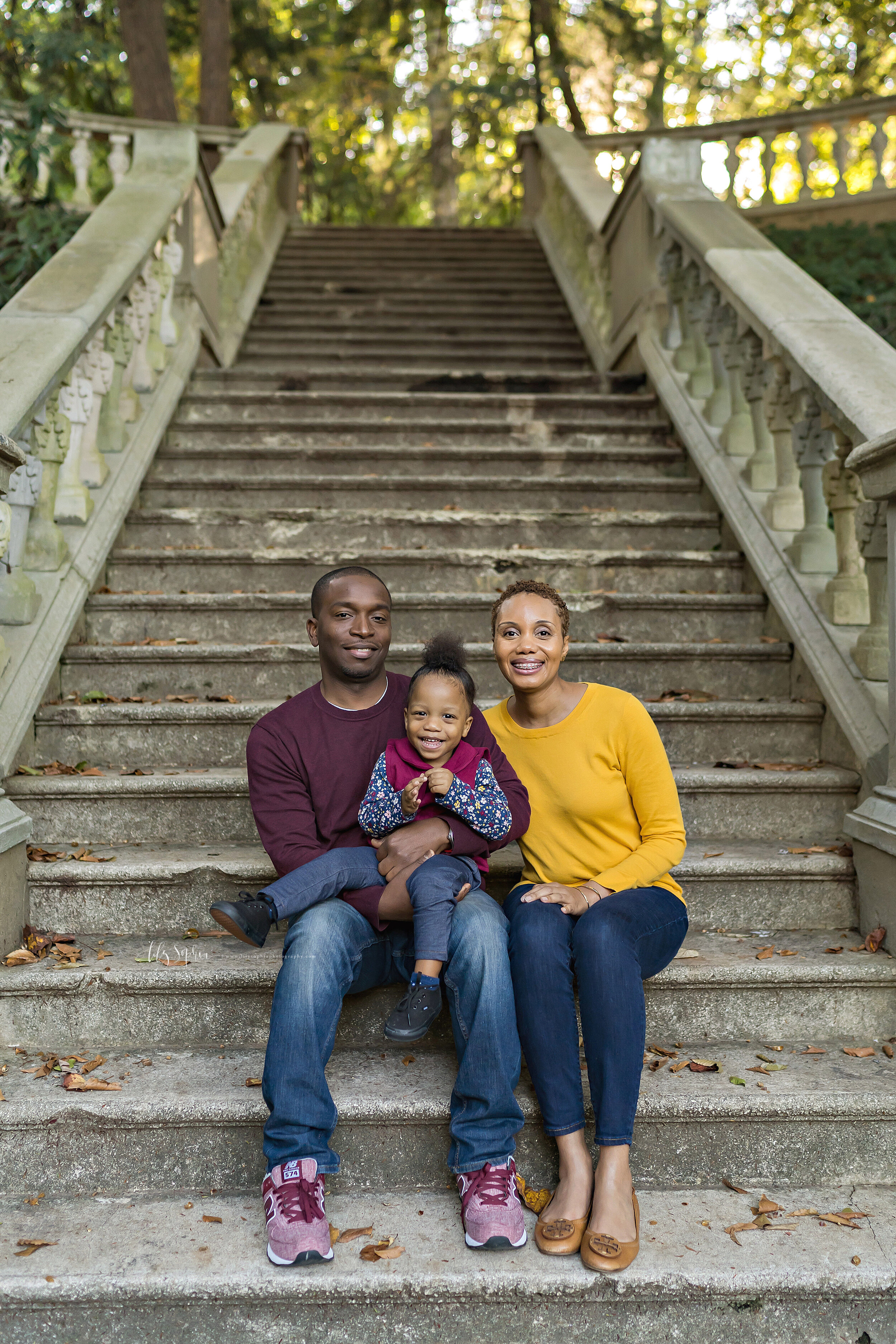  Family photo of an African-American family of three as they sit on a stone staircase at sunset in an Atlanta garden. 