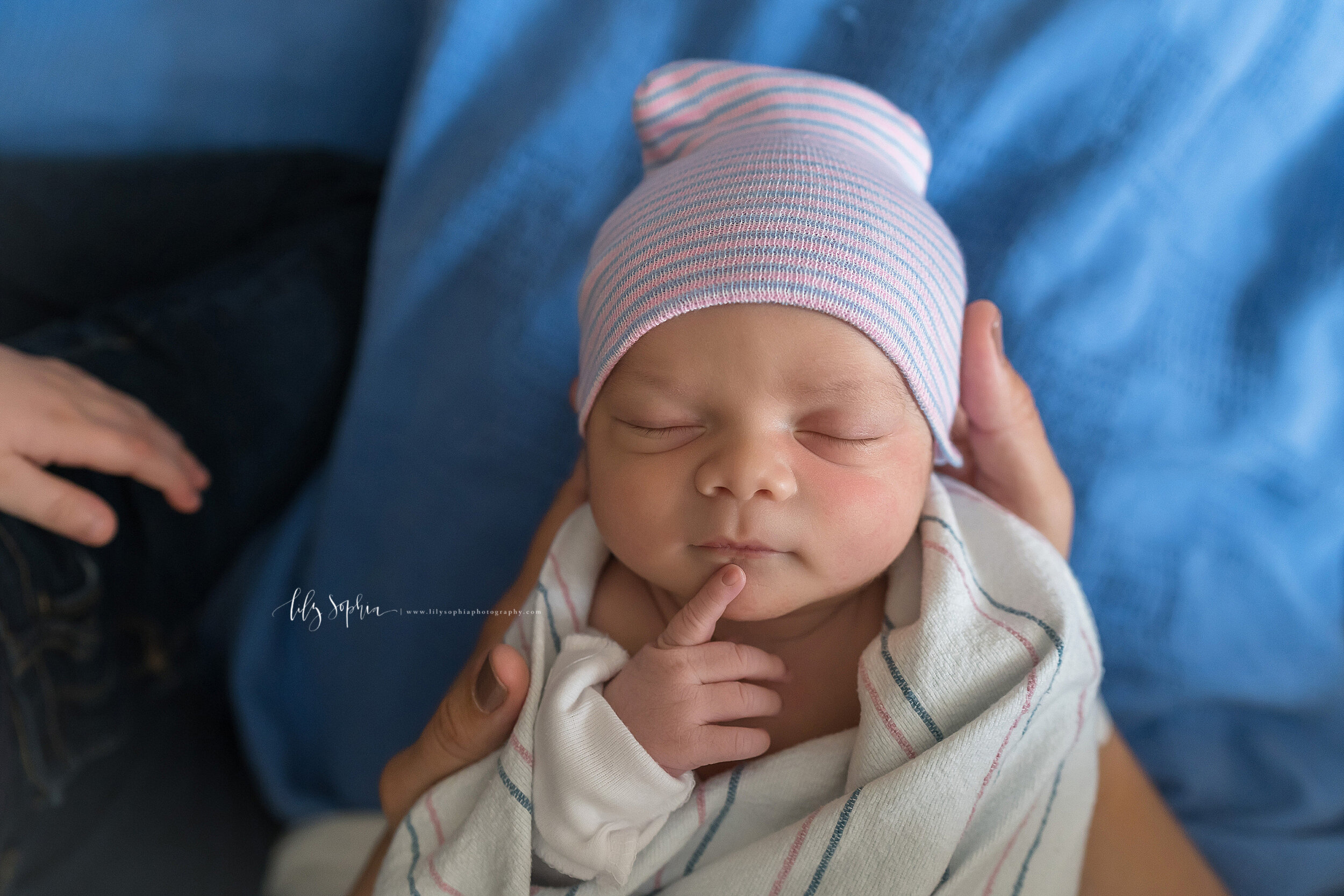  Precious newborn photo of a baby girl with her hospital cap on her head as she touches her chin taken in natural light in an Atlanta hospital within forty-eight hours of her birth. 