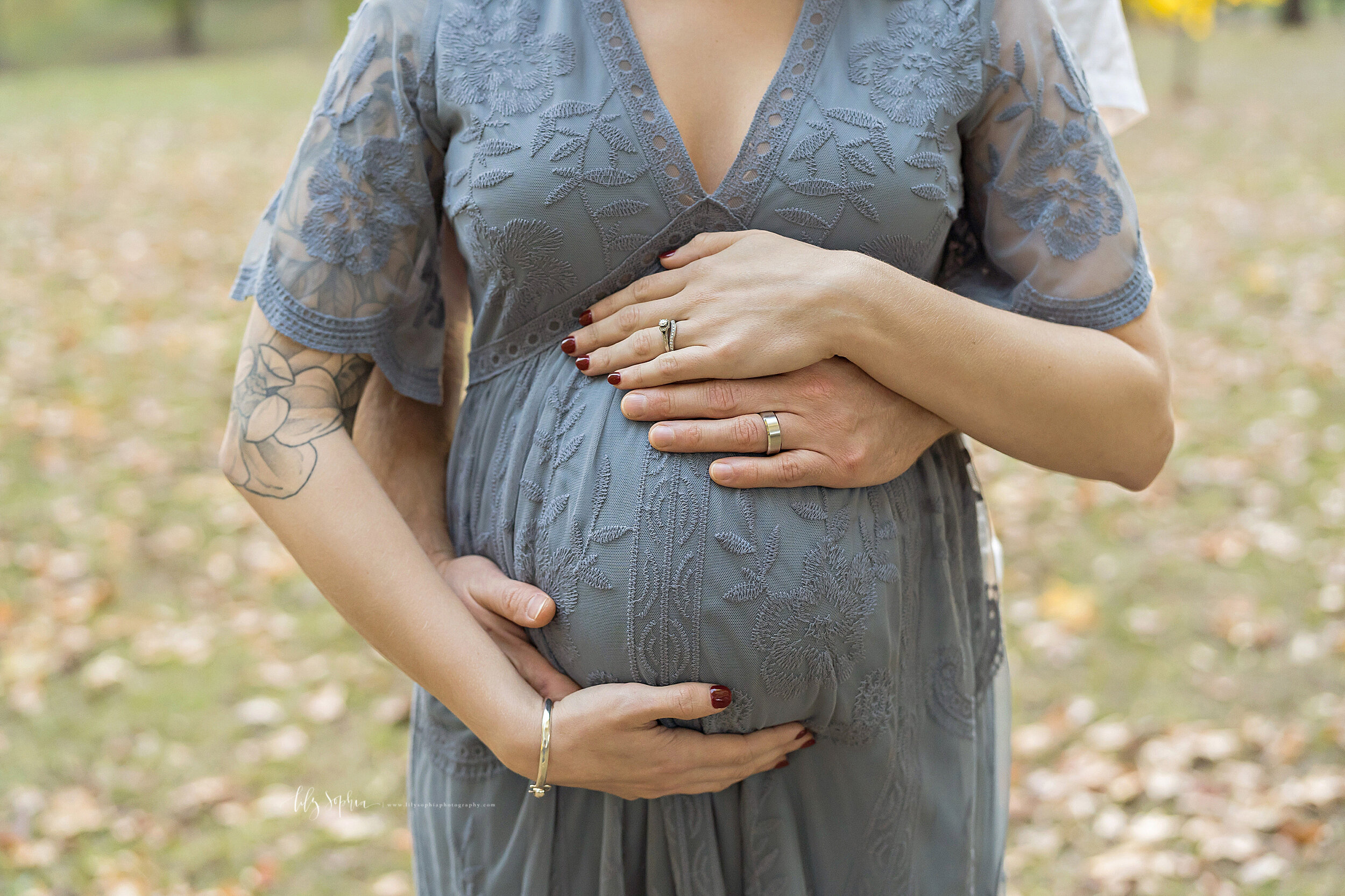  Maternity photo of a close-up of a pregnant woman’s belly as the husband and wife frame their child in utero with their hands as they stand in a park near Atlanta, Georgia during the fall season. 