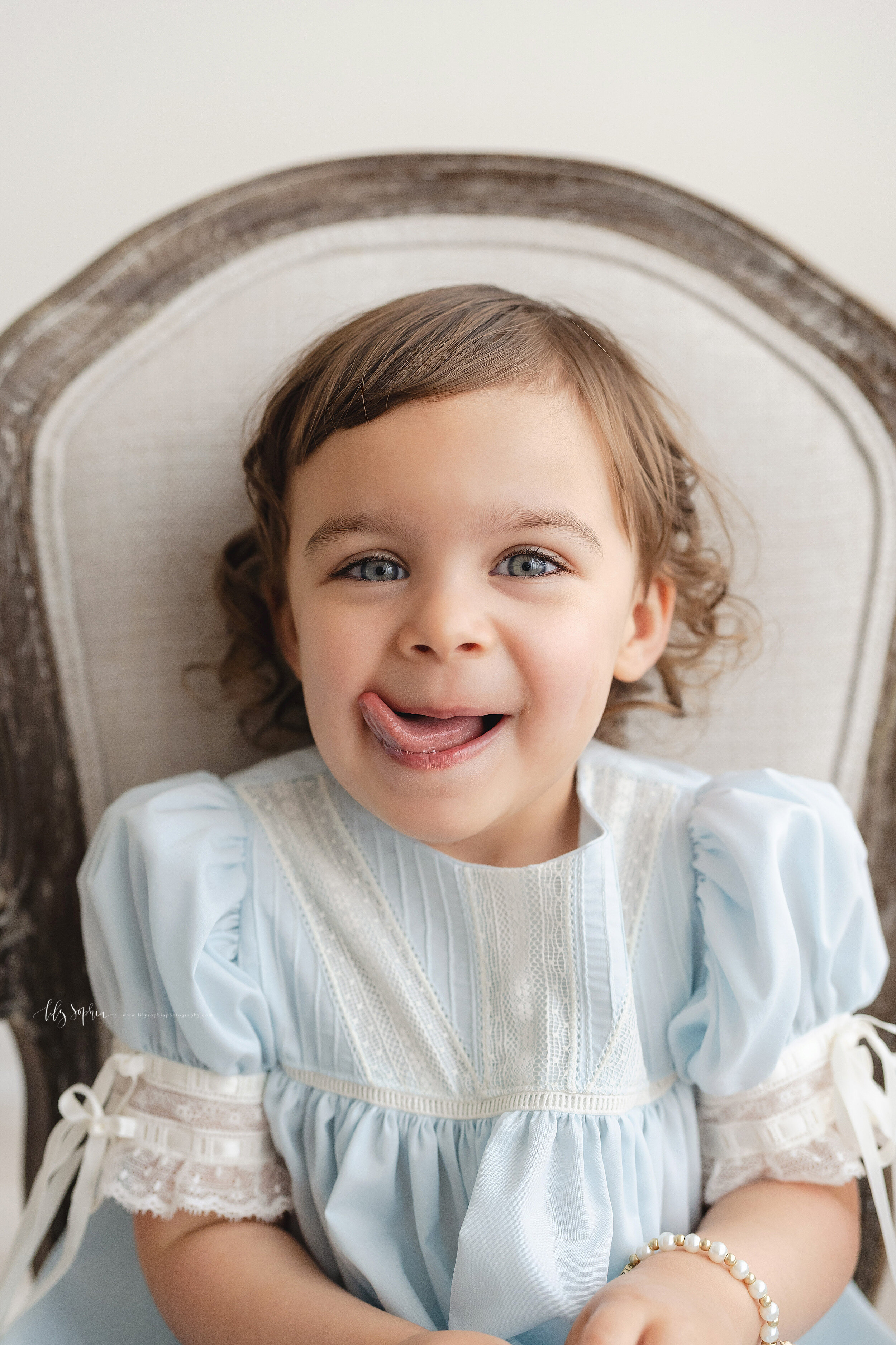  Milestone photo of a two year old girl as she sits in a chair and licks her lips in a natural light studio near the Ansley Park area of Atlanta. 