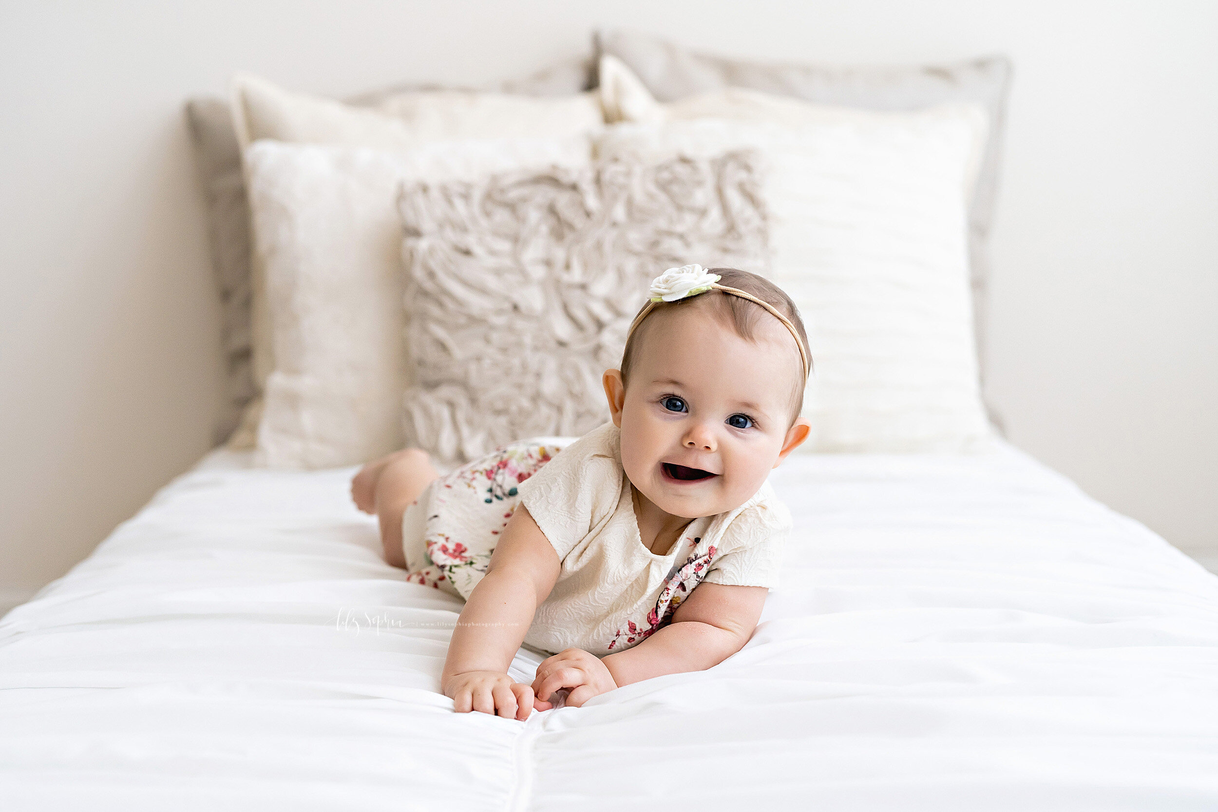  Milestone photo of a wide-eyed baby girl as she lies on her tummy on a bed in natural light in a studio in the Peachtree HIlls area of Atlanta. 