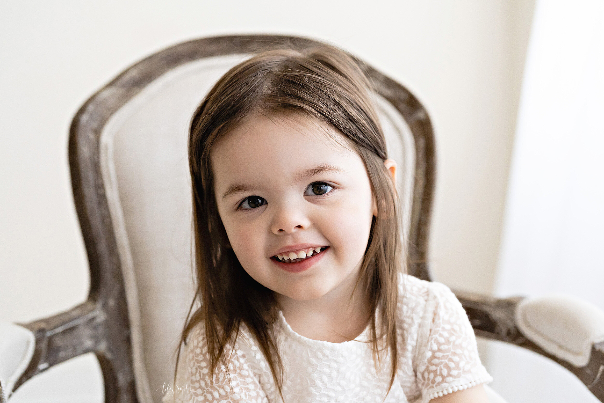  Milestone photo of a toddler girl as she sits in an armchair in front of a natural light window in a Candler Park studio in Atlanta. 