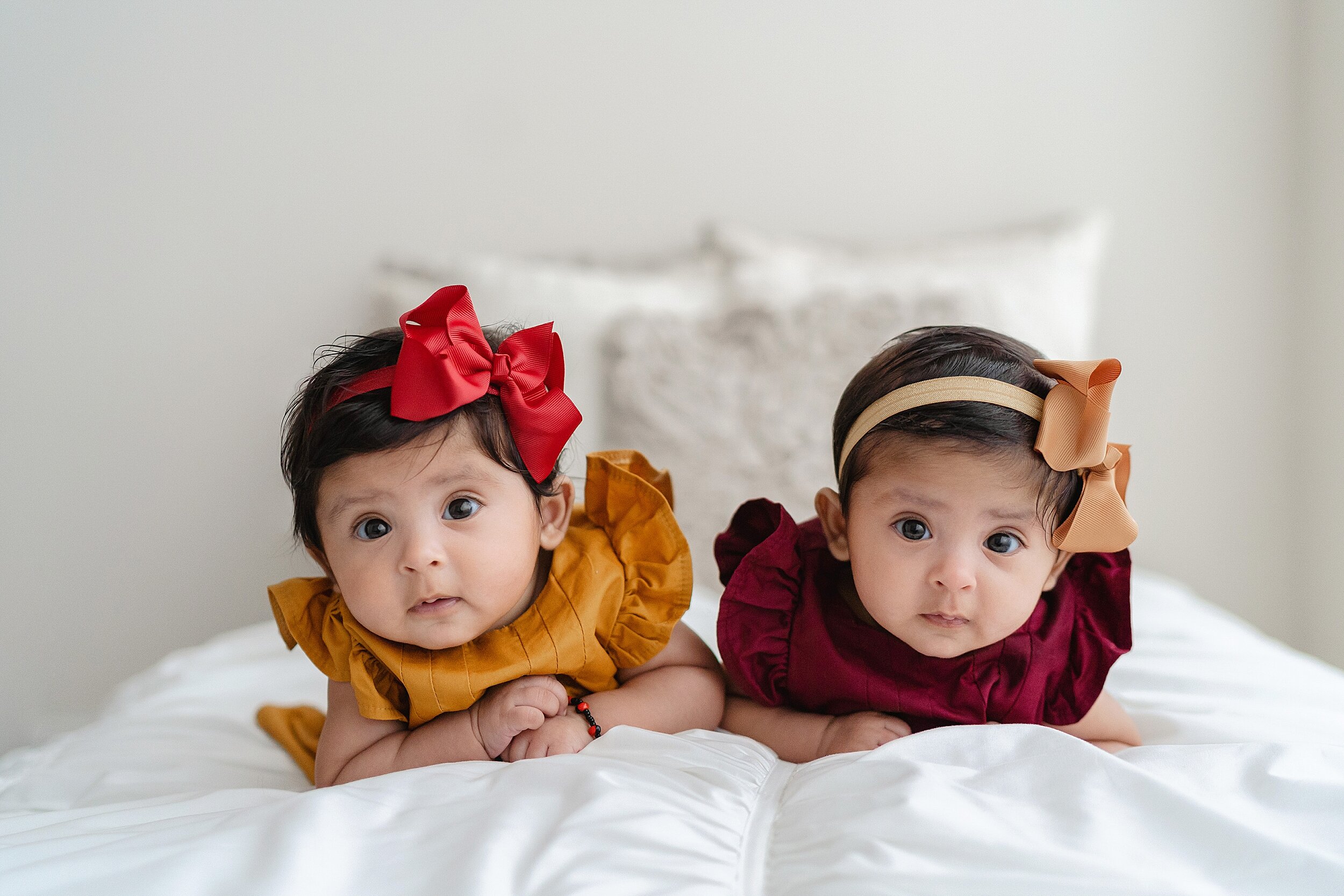  Baby photograph of twin girls lying on their stomachs in natural light wearing bow headbands in their hair in an Atlanta studio near Inman Park. 