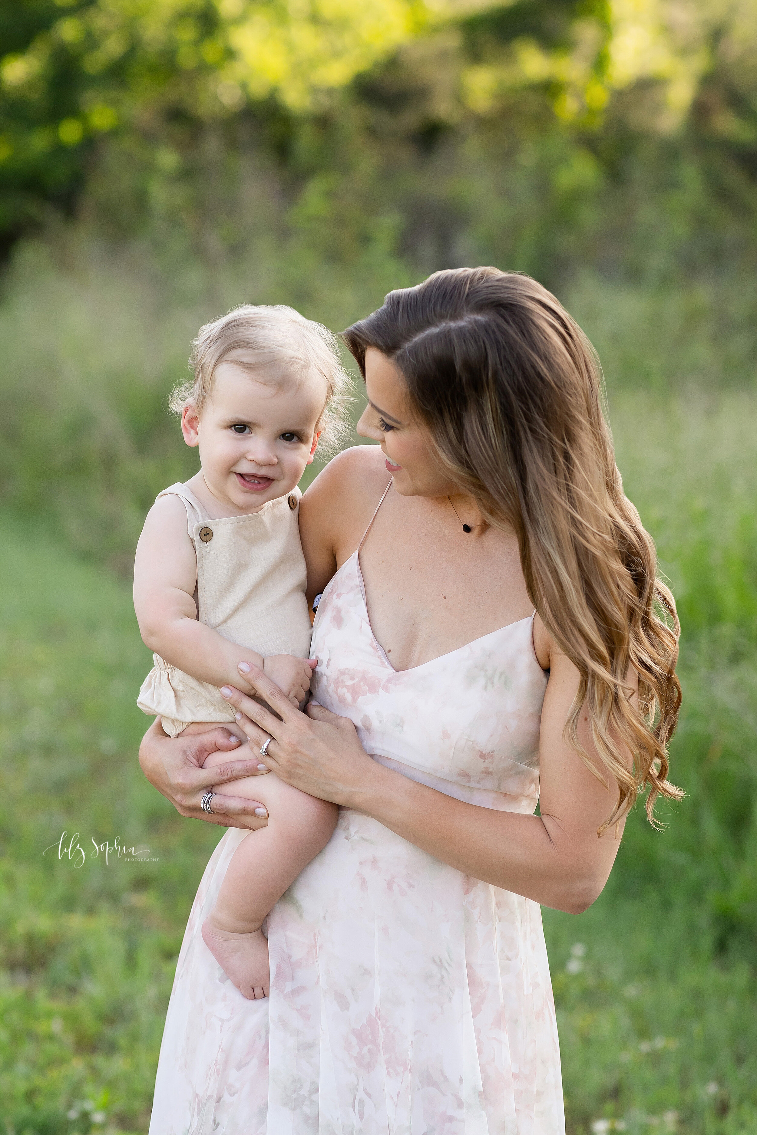  Family photo of mom holding her baby boy on her right hip as they stand in a field at sunset during the summer in Atlanta. 