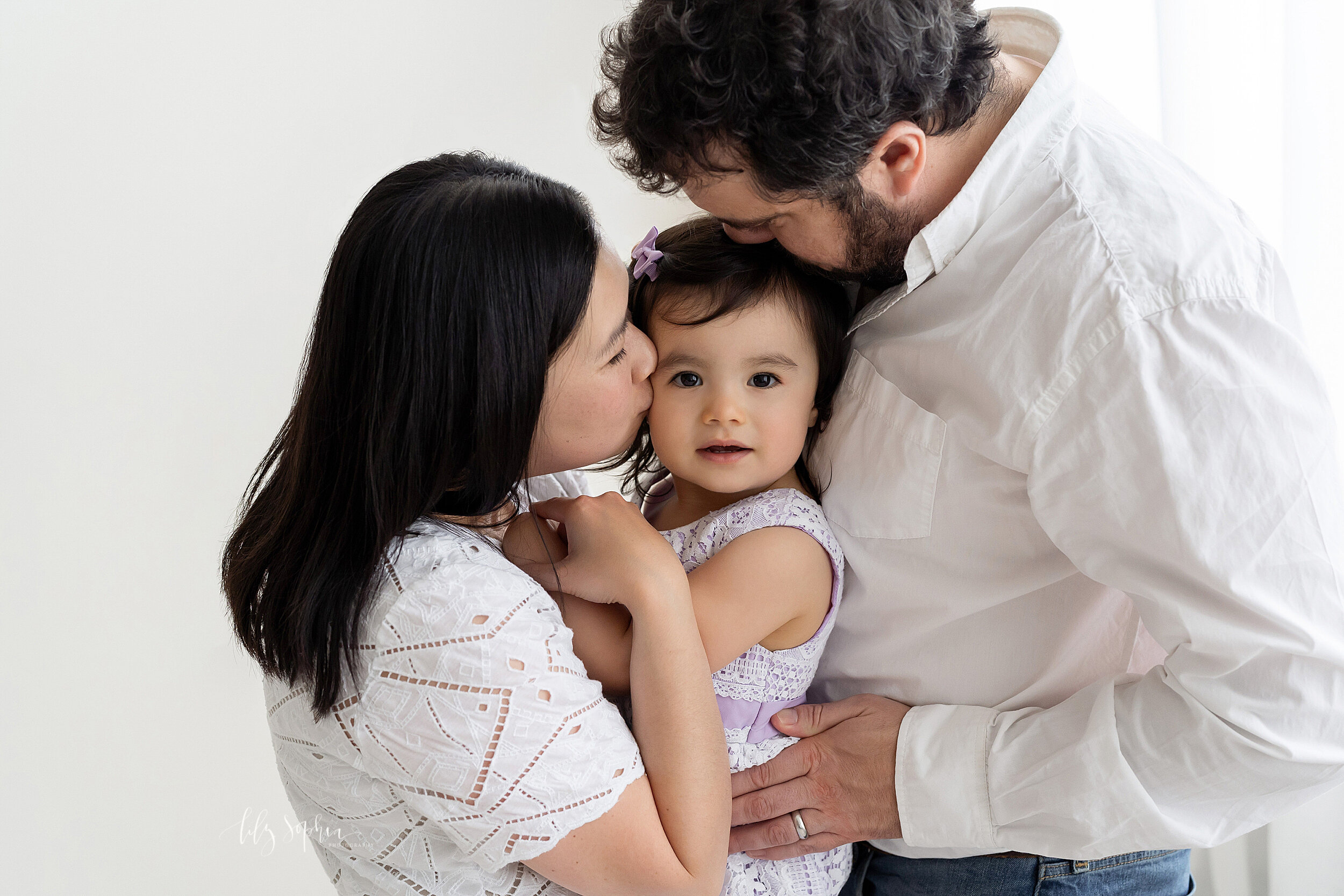  Family photo of a mother, father, and their two-year old daughter taken in a natural light studio in the Candler Park area of Atlanta. 