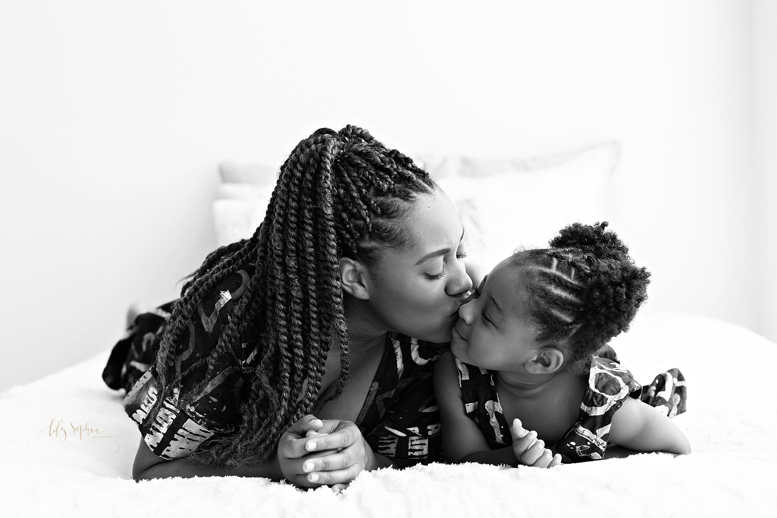  Black and white family photo of an African-American mom lying next to her daughter on their stomachs with mom kissing her daughter on the cheek taken near the Buckhead area of Atlanta. 