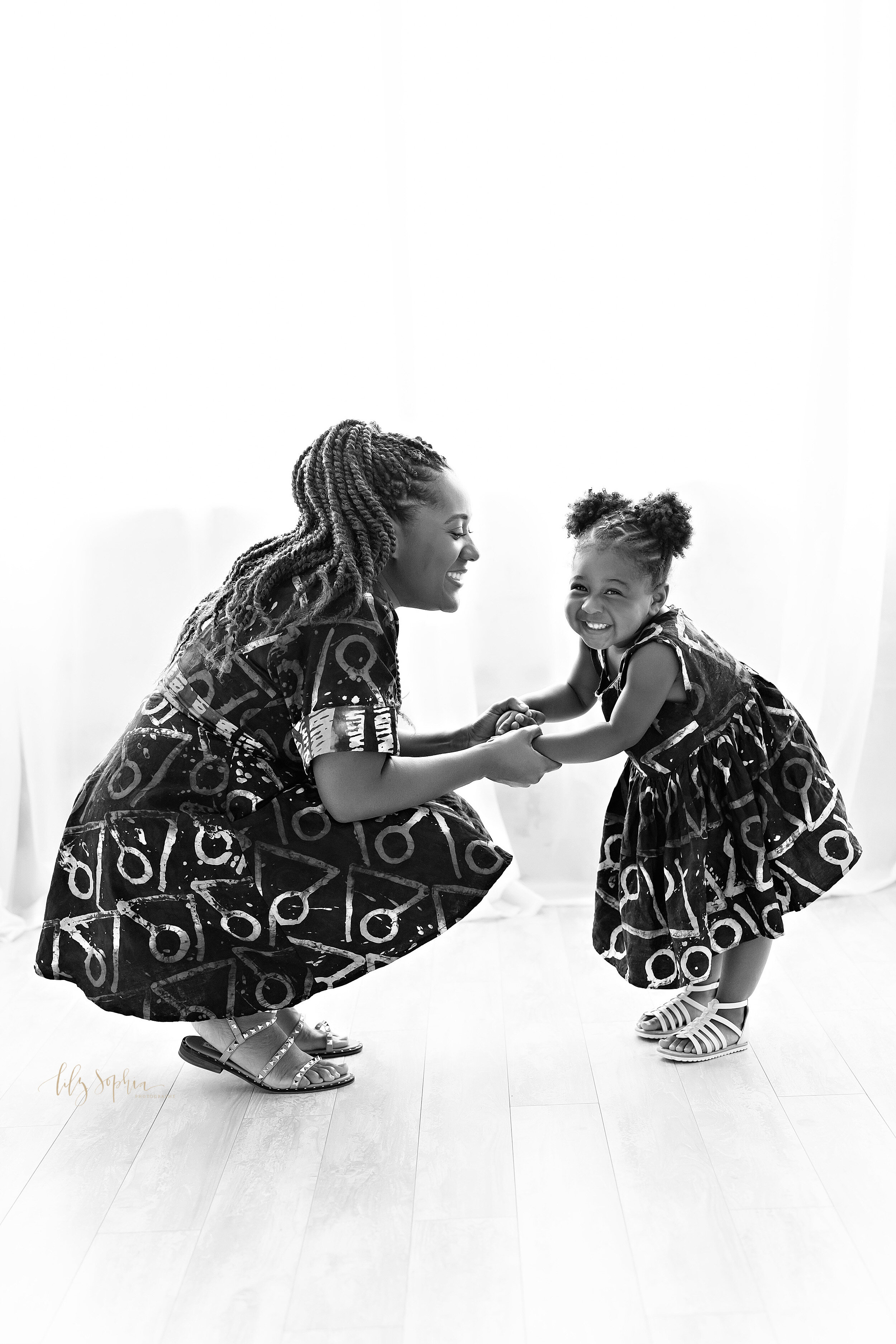  Natural black and white picture of an African-American mom squatting in front of her toddler daughter as they hold hands and the toddler giggles taken in a studio near the Ansley Park area of Atlanta, Georgia. 