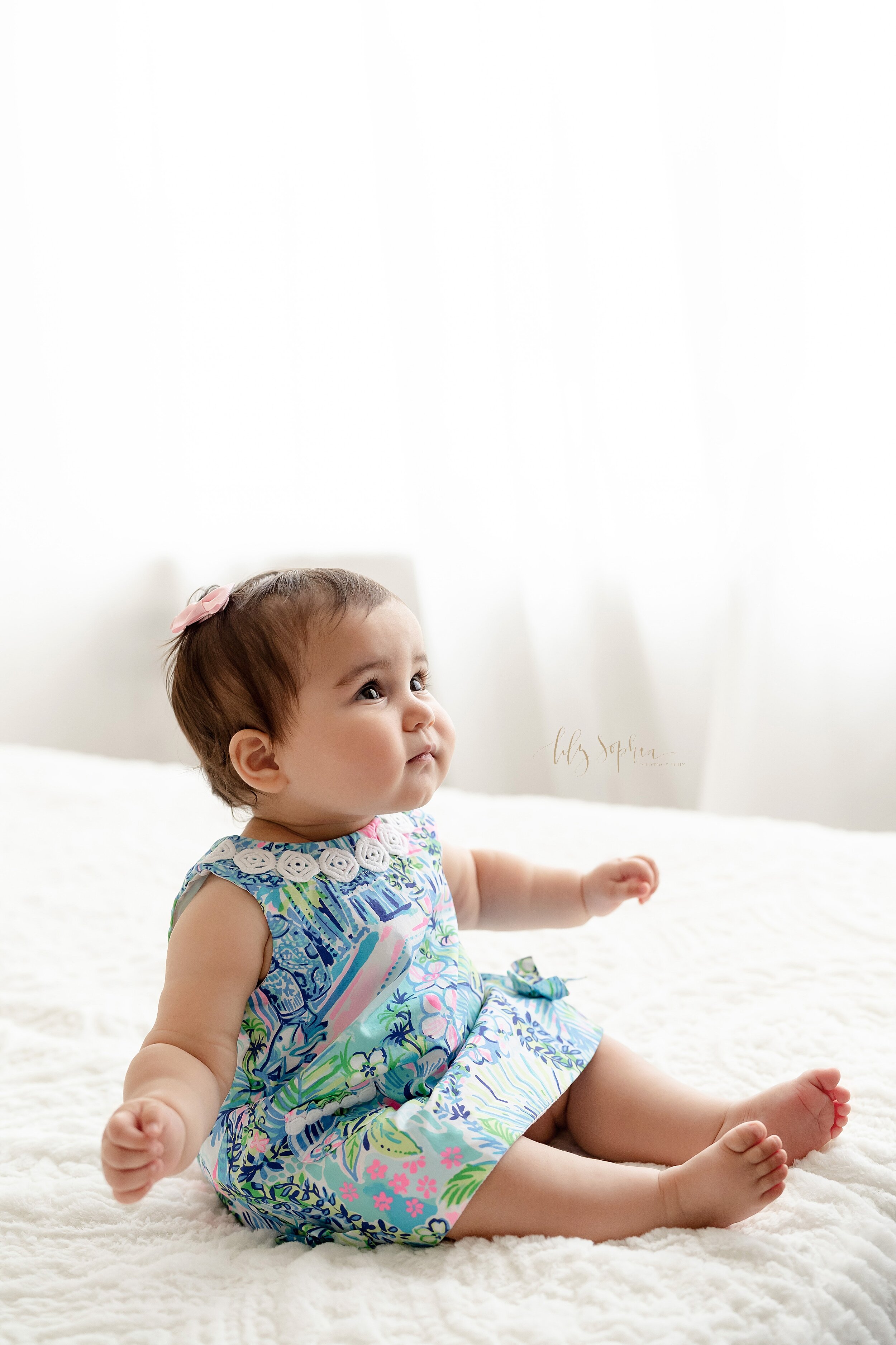  First birthday photo of a little girl as she sits on a bed in front of a window streaming natural light in a studio near the Candler Park area of Atlanta. 