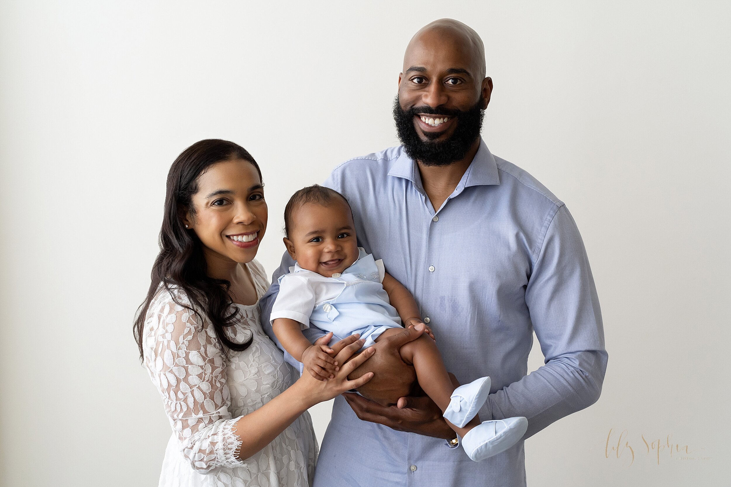  Family portrait of an African-American father holding his six month old son with mom standing beside her husband taken in a studio near the Kirkwood area of Atlanta in natural light. 