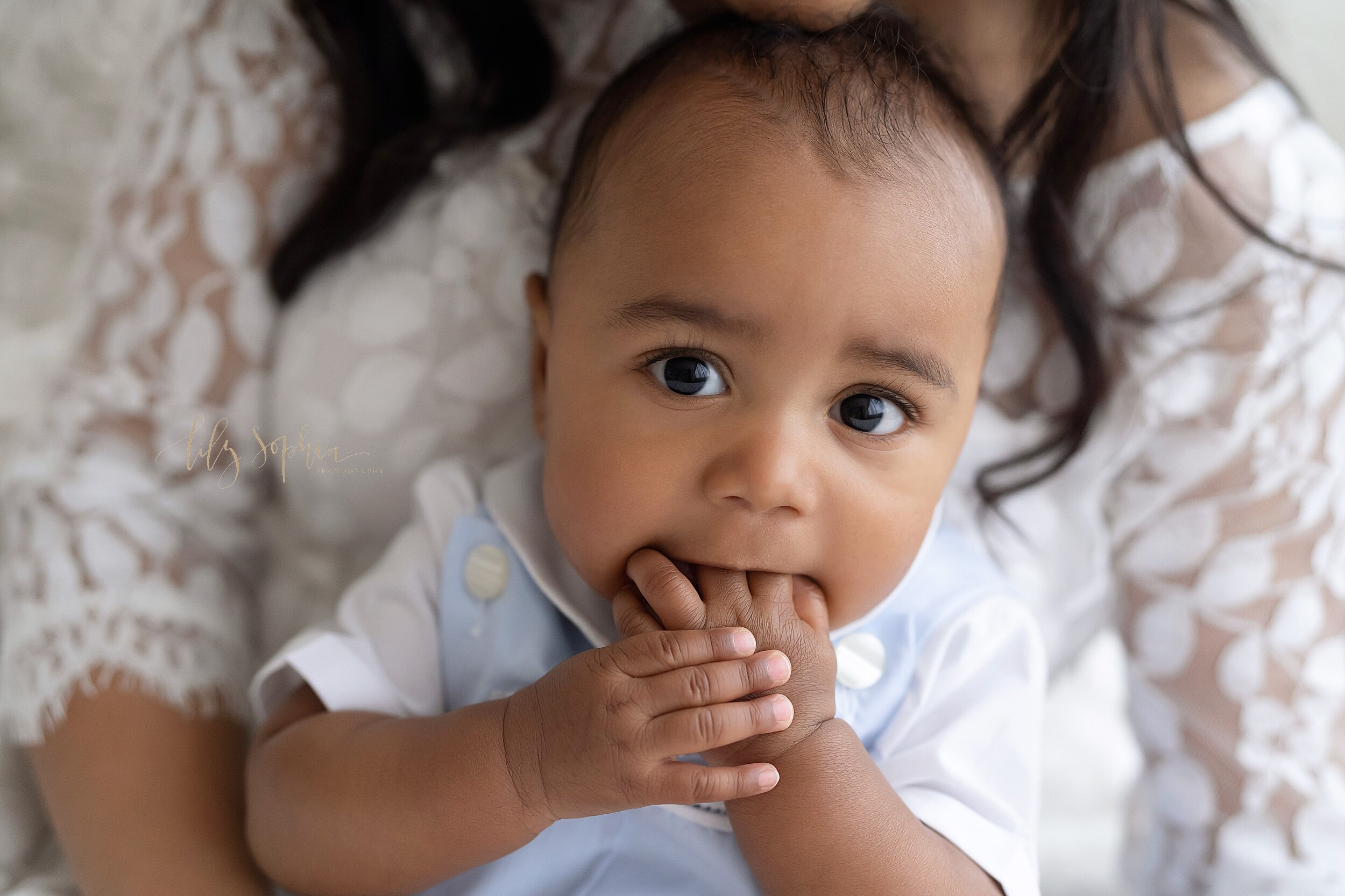  Baby photo of an African-American six month old boy as he sits on his mother’s lap and eats his fingers taken in a natural light studio in the Ponce City Market in Atlanta, Georgia. 