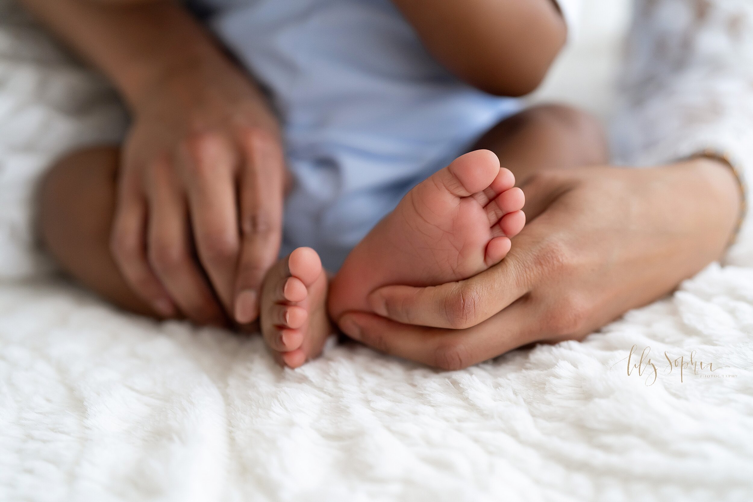  Close-up photo of the tiny feet of a six month old African-American baby as he sits with his mother on a bed and she holds his feet taken in natural light in a studio near the Candler Park area of Atlanta. 