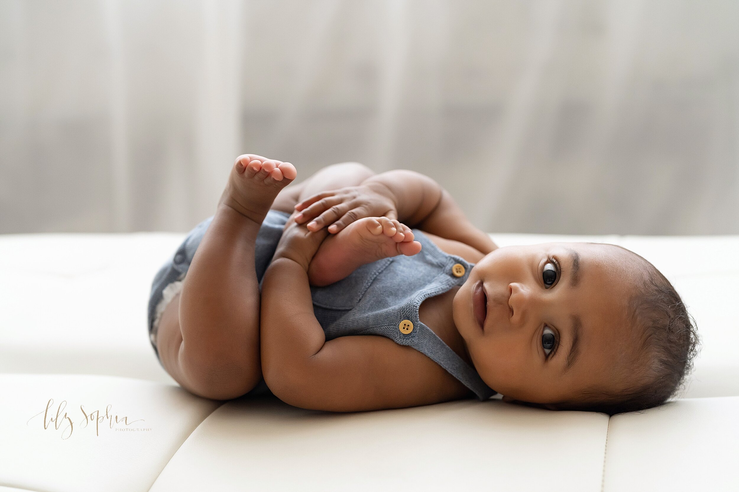  Baby picture of a six month old African-American boy as he lies on his back and plays with his foot in front of a natural light window in a studio near the Old Fourth Ward area of Atlanta. 