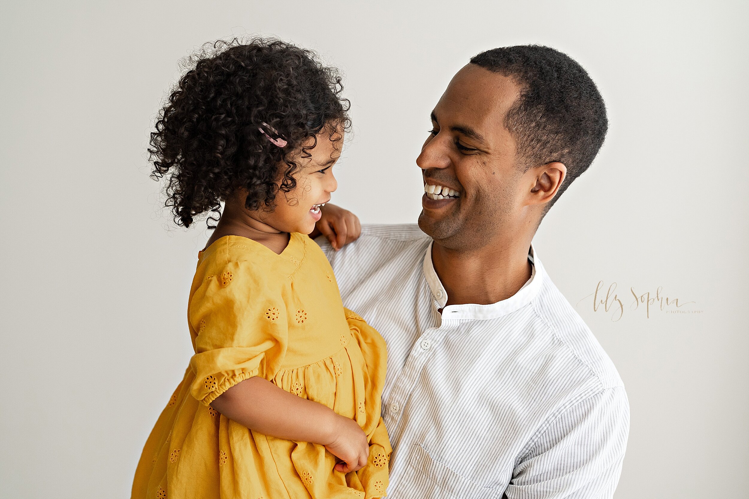  Family photo of an African-American dad holding his daughter as they two of them laugh together taken in natural light in a studio in the Ponce City Market in Atlanta, Georgia. 