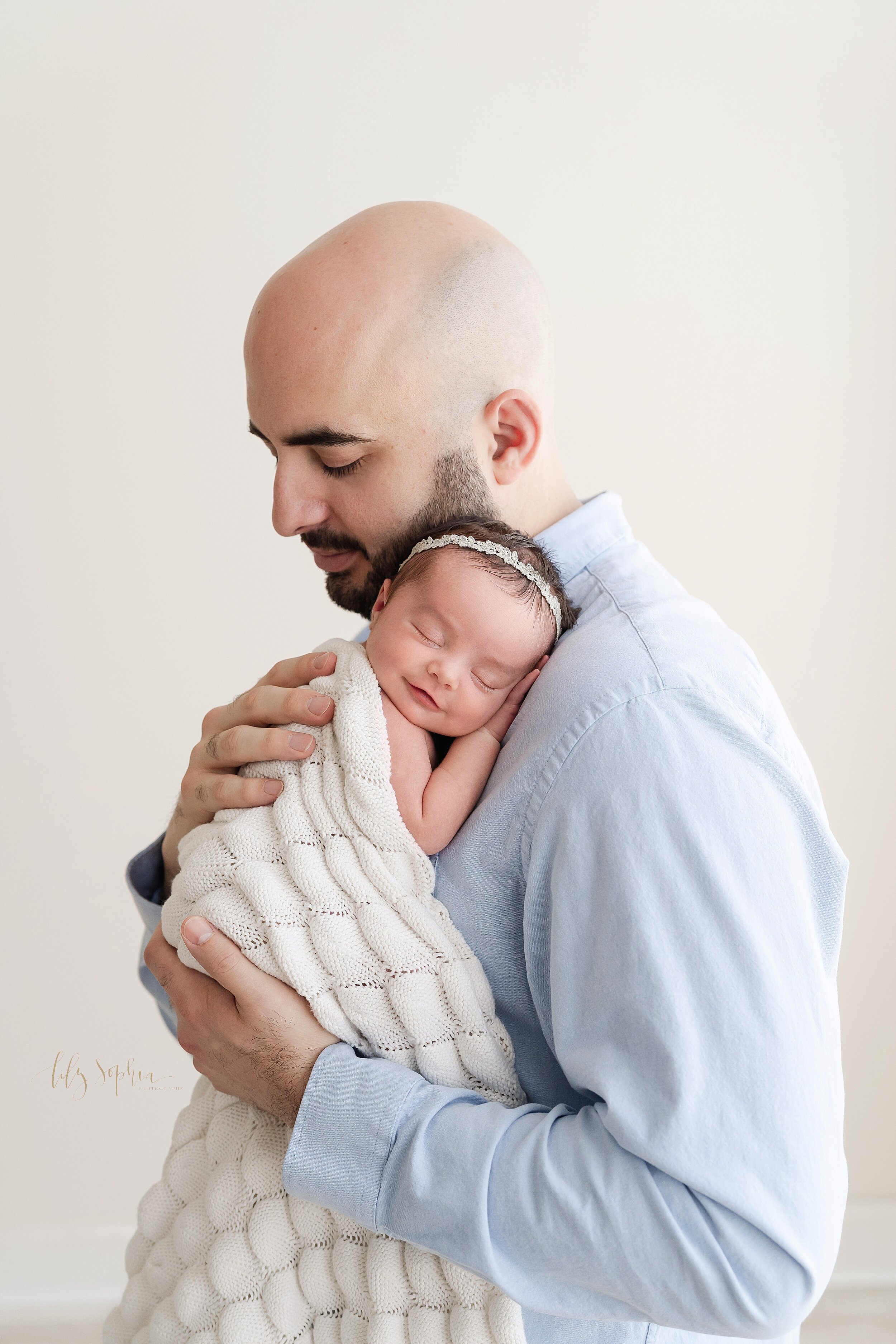  Newborn photo of a father holding his precious baby girl on his shoulder as she grins and he treasures this time with her taken in a natural light studio near Virginia Highlands in Atlanta. 