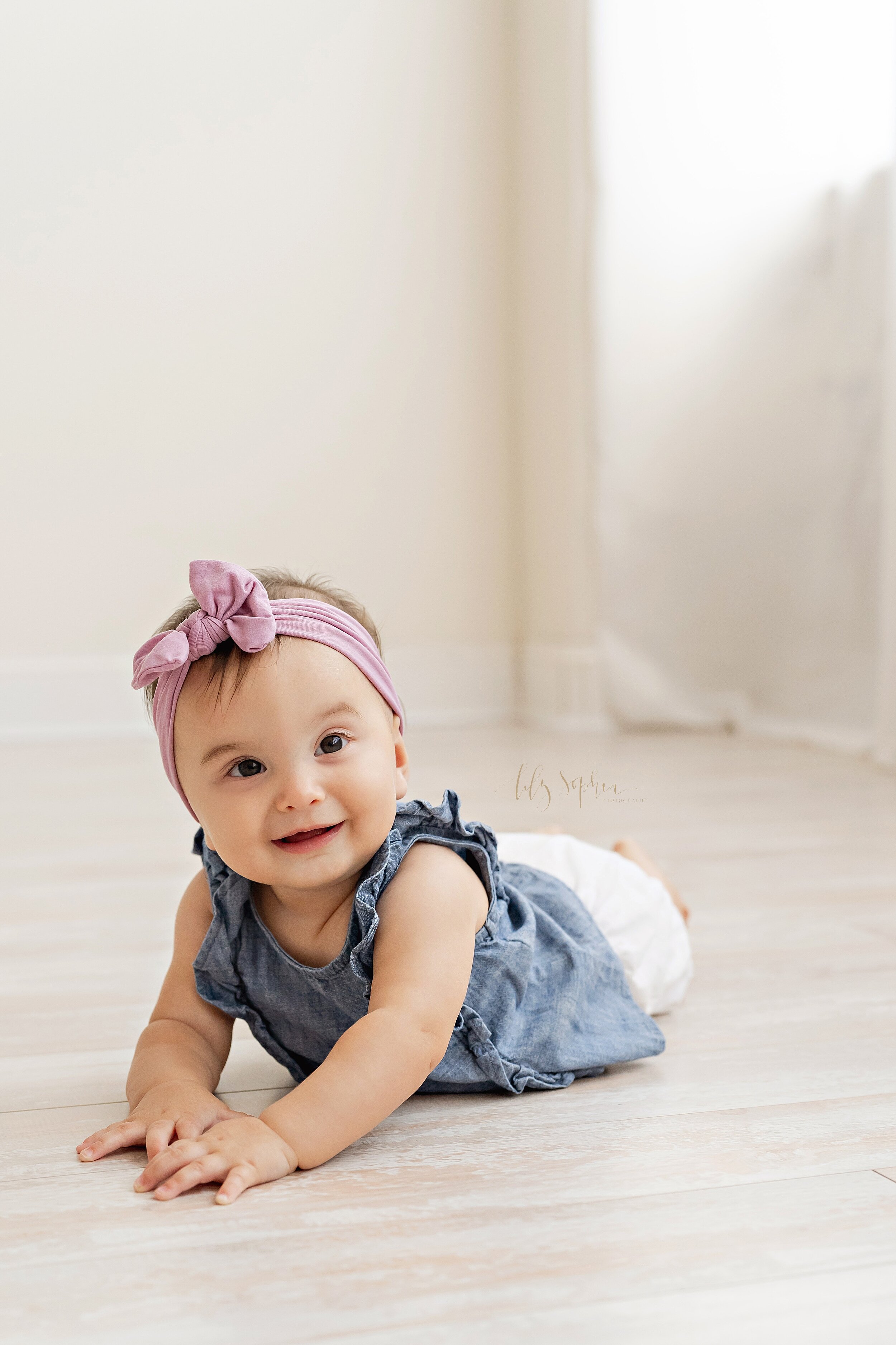  Baby picture of a six-month old little girl as she crawls along the wooden floor of a natural light studio near Alpharetta in Atlanta. 