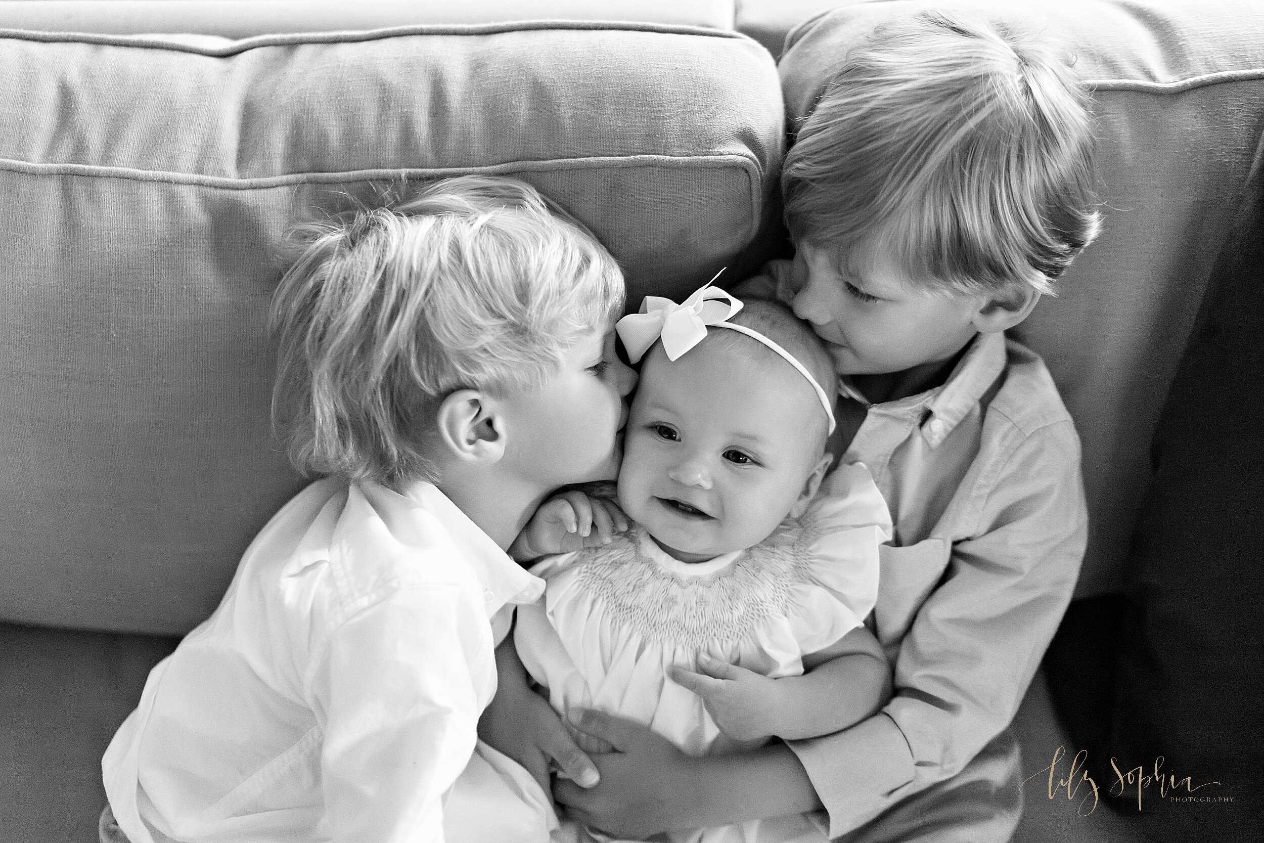  Family photo of siblings sitting on a sofa in their home in Atlanta as the eldest brother holds his six month old sister on her lap and the other brother kisses his sister on the cheek. 