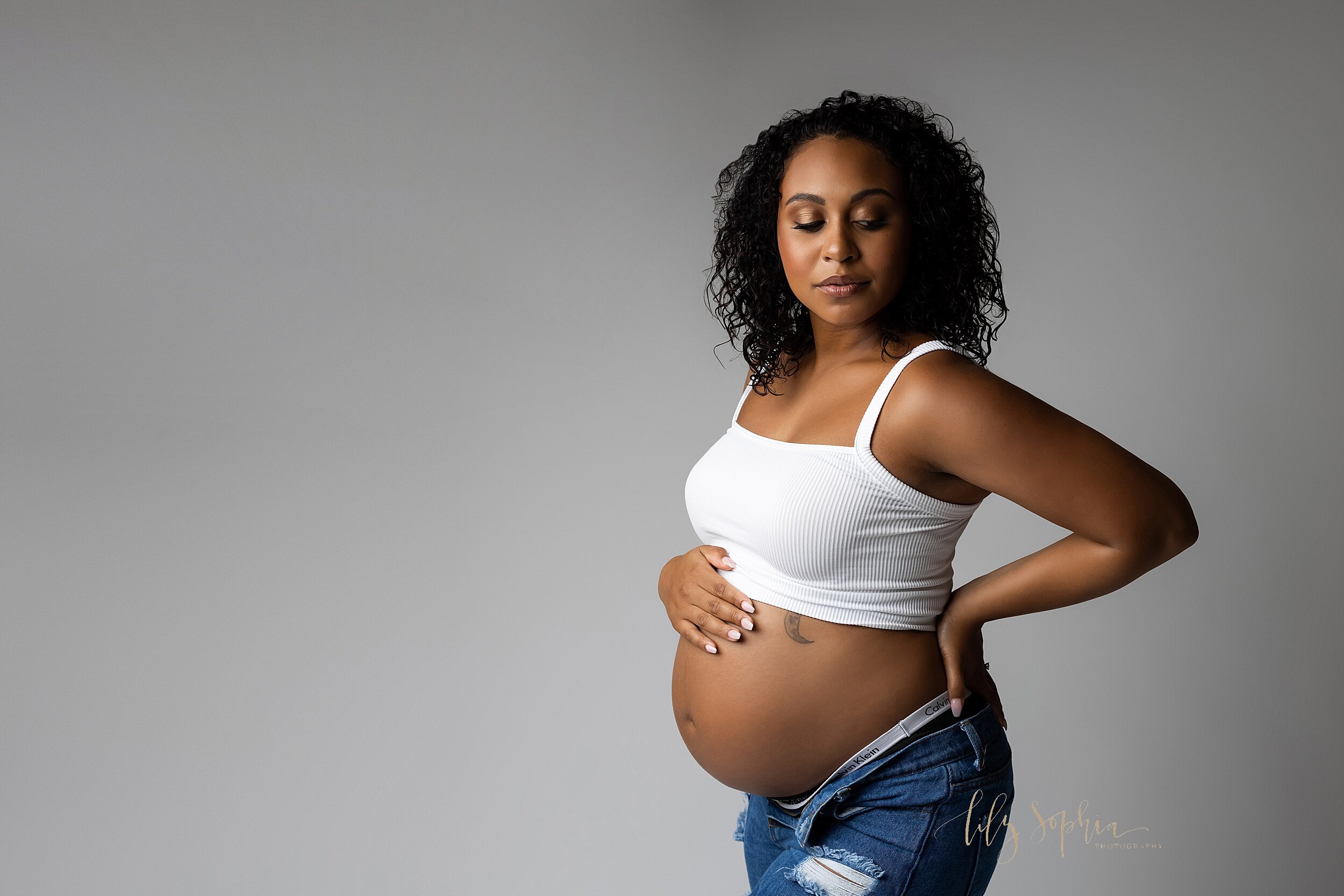  Modern maternity images of a confident black pregnant woman wearing white crop top and ripped jeans. Taken by Lily Sophia Photography located in Atlanta.  