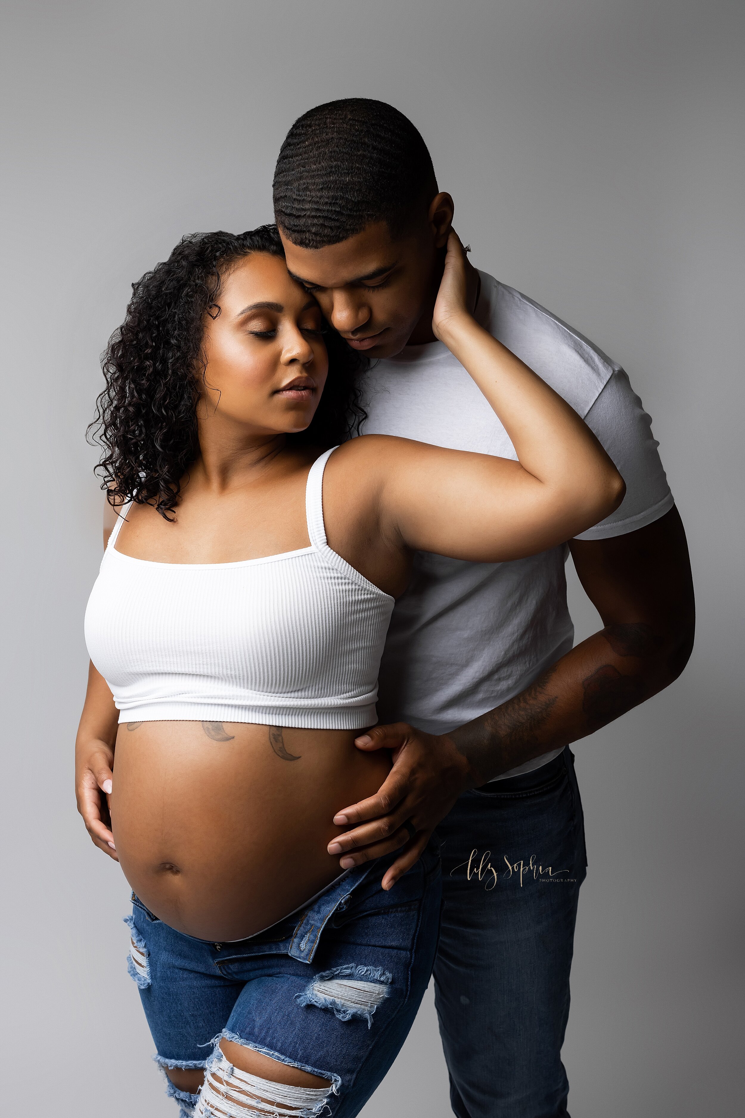  Modern studio portrait of a black expectant couple in Atlanta, Georgia.  The mother caresses her partner’s face as he gently holds her pregnant belly.  