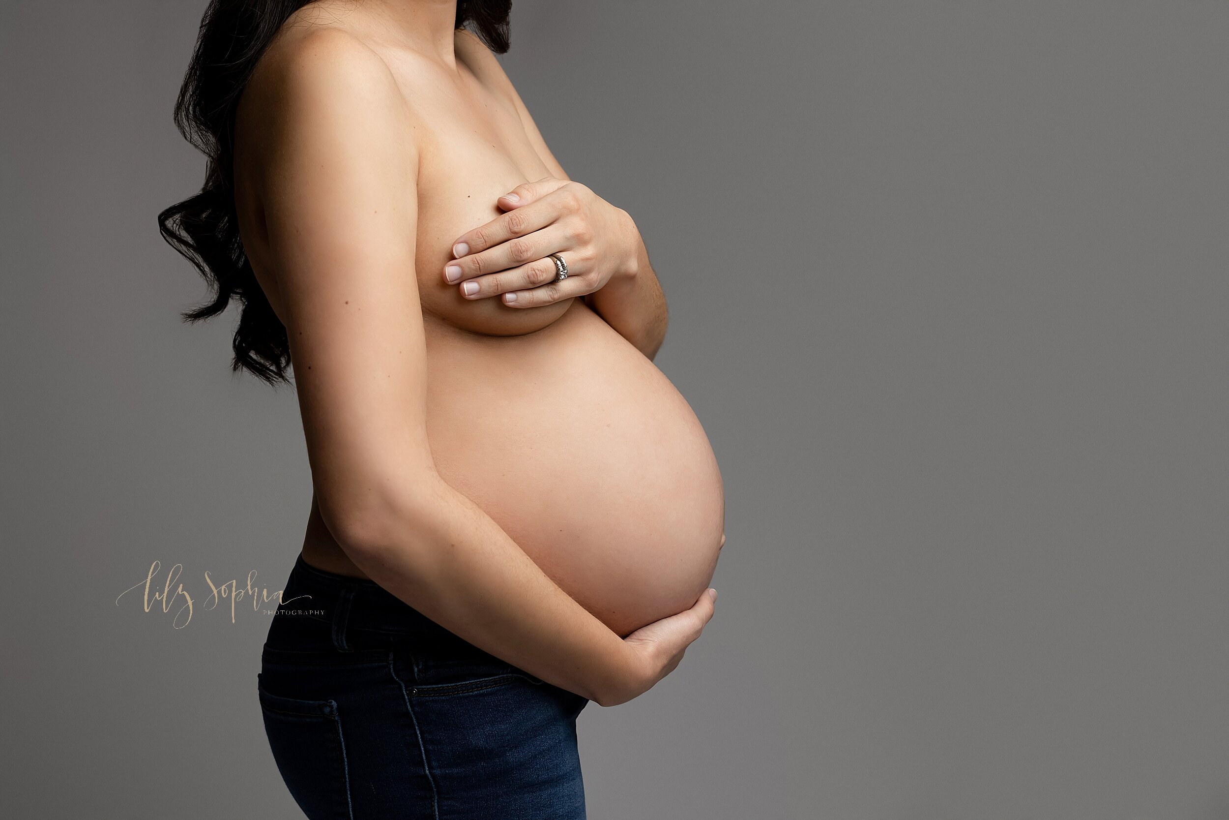  Atlanta Fine art modern maternity portrait of pregnant woman wearing jeans and holding her baby belly with strategic hand placement over her breasts.  