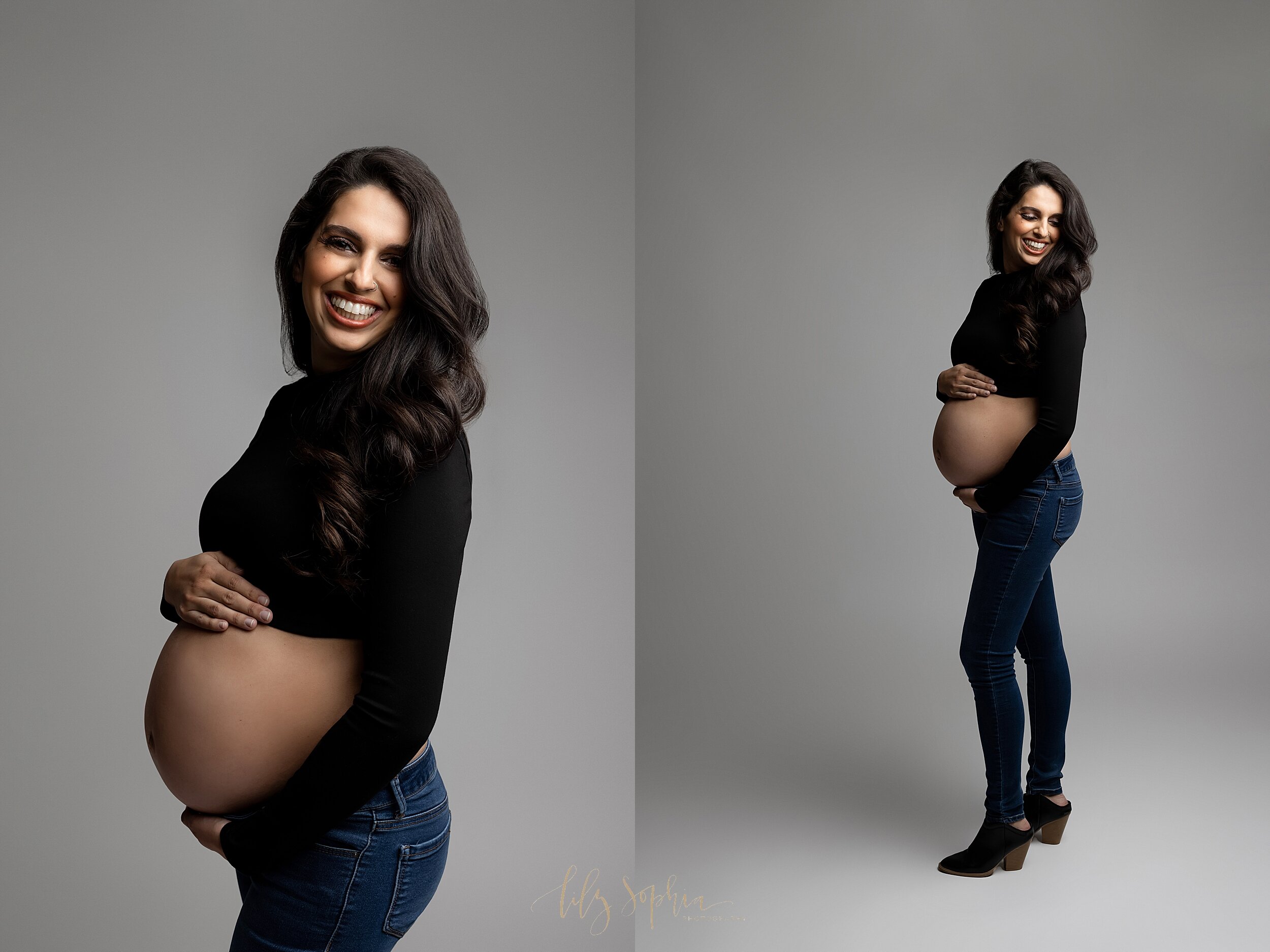  Fine art maternity Atlanta studio portrait of smiling pregnant woman with long brown hair wearing skinny jeans and black turtleneck crop top while cradling her baby bump. 