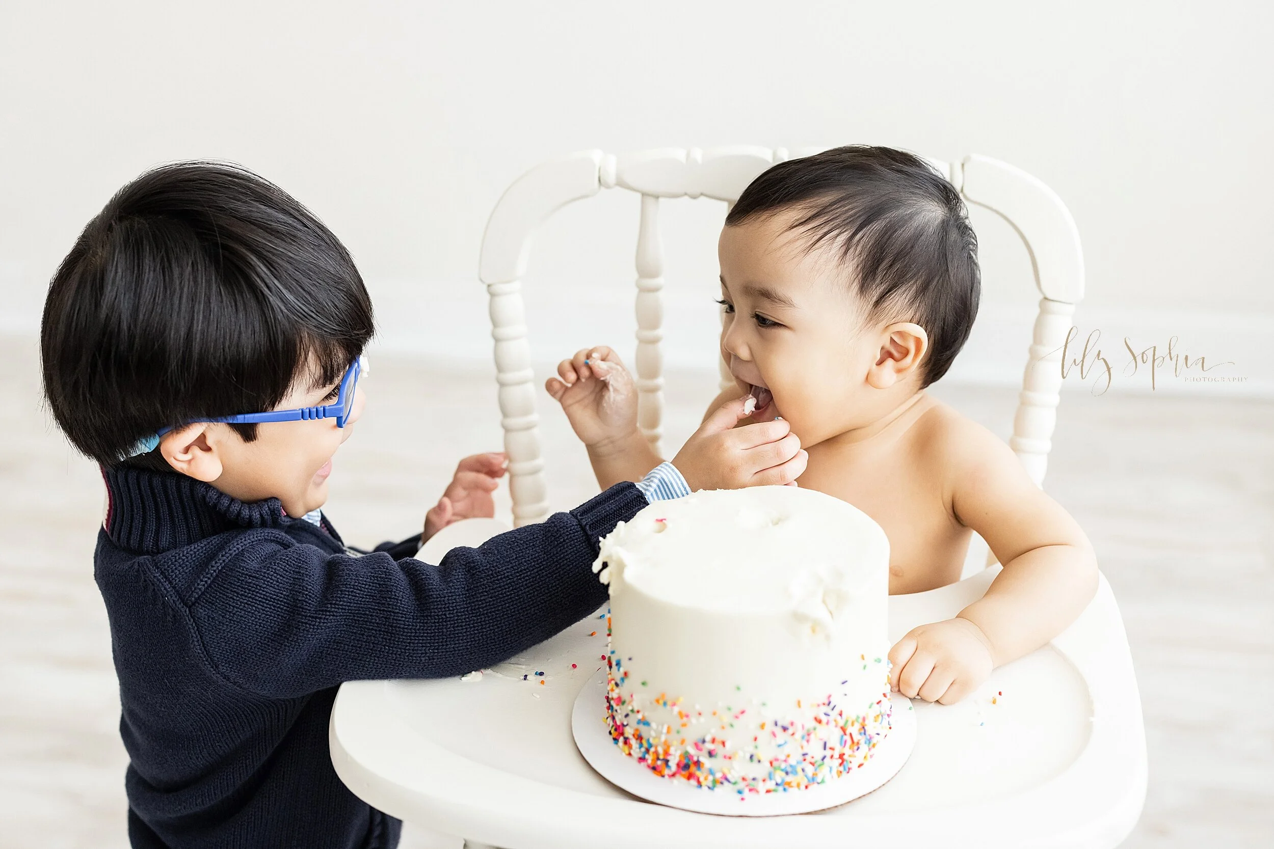  Milestone photo of a one-year old Asian baby boy as he and his older brother enjoy his smash cake for his birthday taken in a studio near Decatur, Georgia using natural light. 