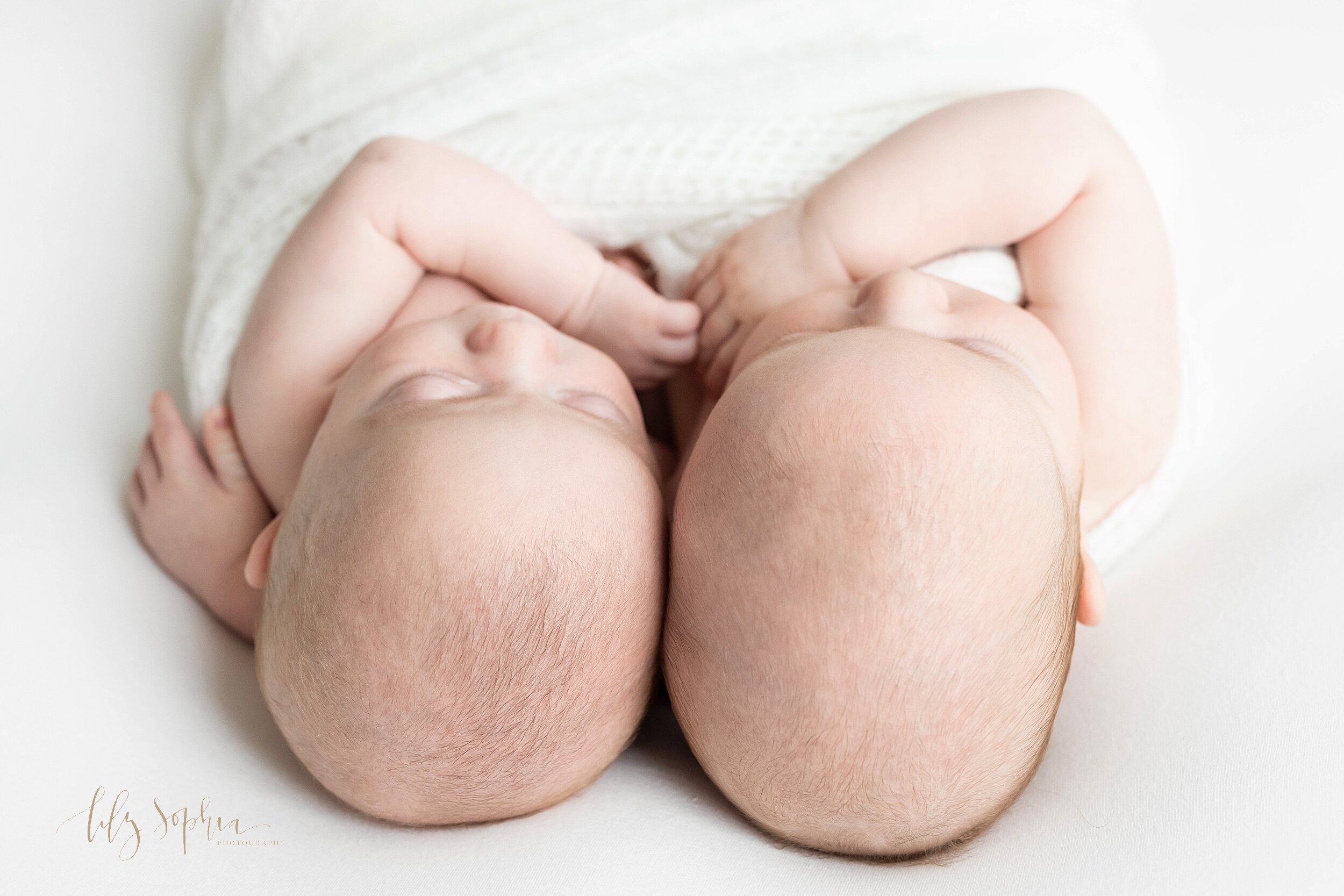  Newborn portrait of twin boys as they lie next to one another on their backs with one of the twins placing his hand around his brother taken in a studio near Morningside in Atlanta using natural light. 