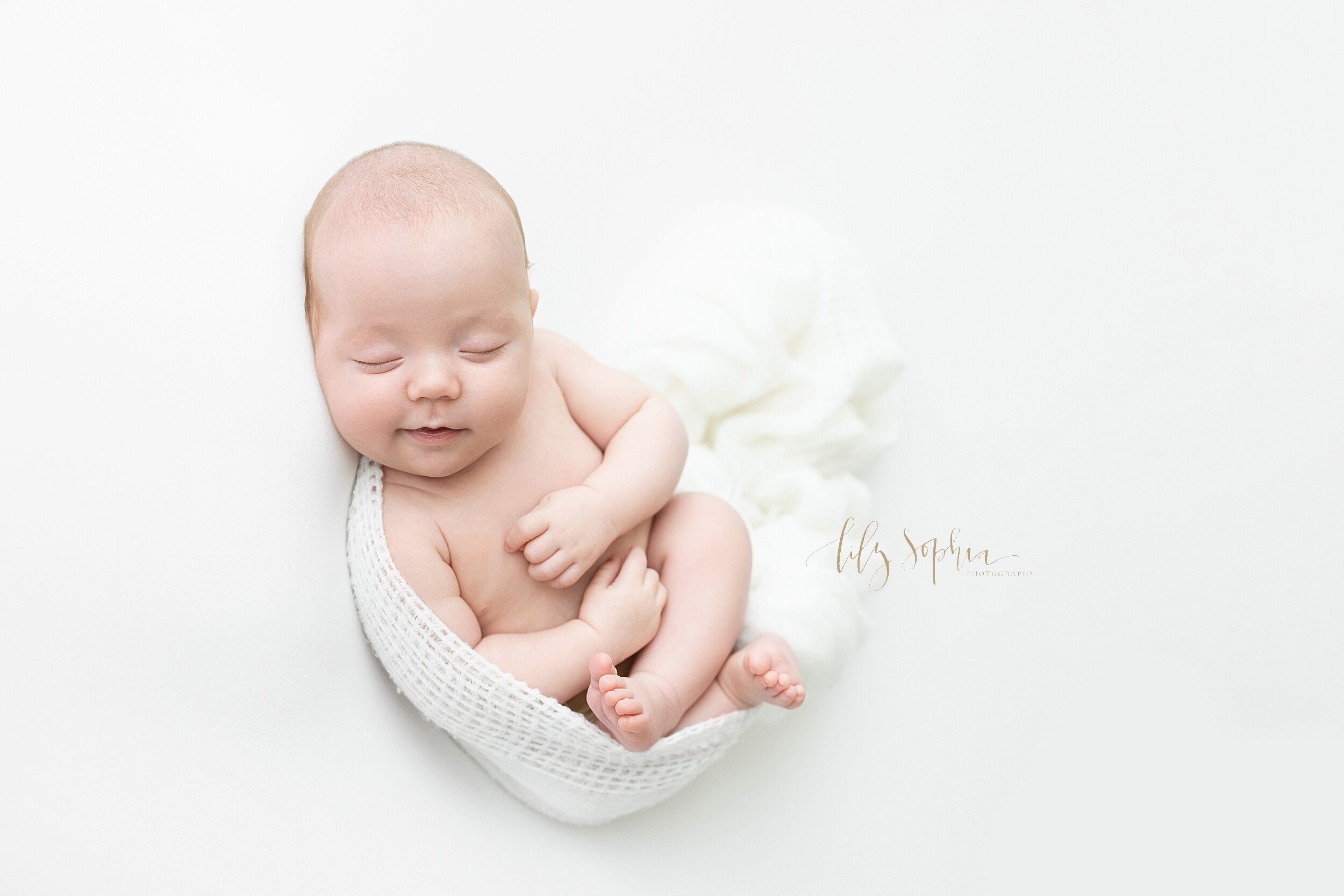 Newborn portrait of an smirking infant boy who is cradled in a soft knit blanket taken in a studio near Cummings, Georgia using natural light. 
