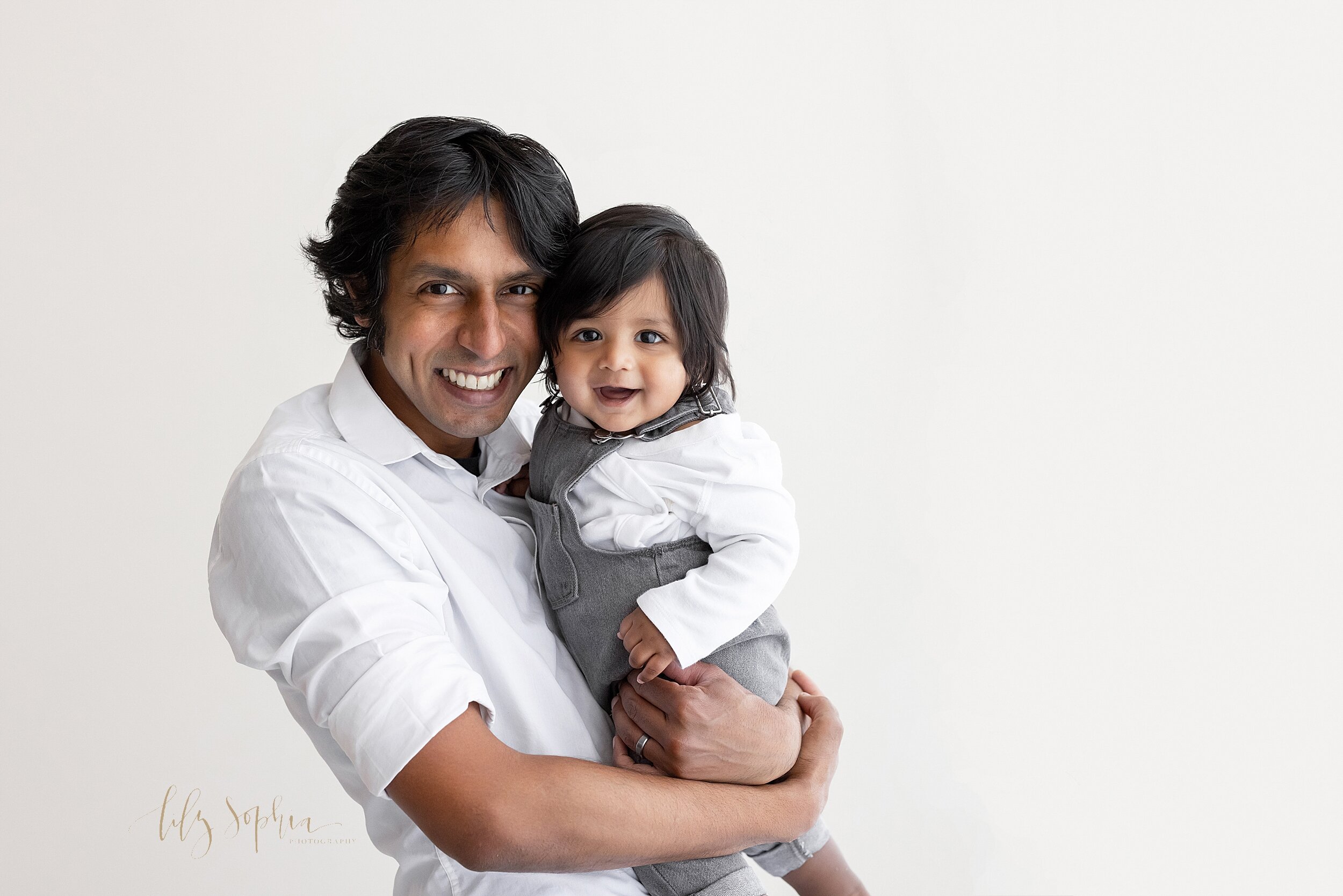  Family portrait of a father holding his six month old son in his arms as he stands in a natural light studio near Midtown in Atlanta. 