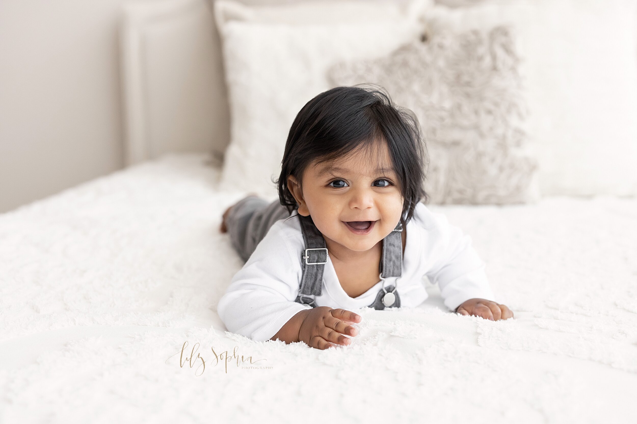  Milestone photograph of a smiling six month old boy lies on his stomach on a bed in a studio near the Morningside area of Atlanta, Georgia in natural light. 