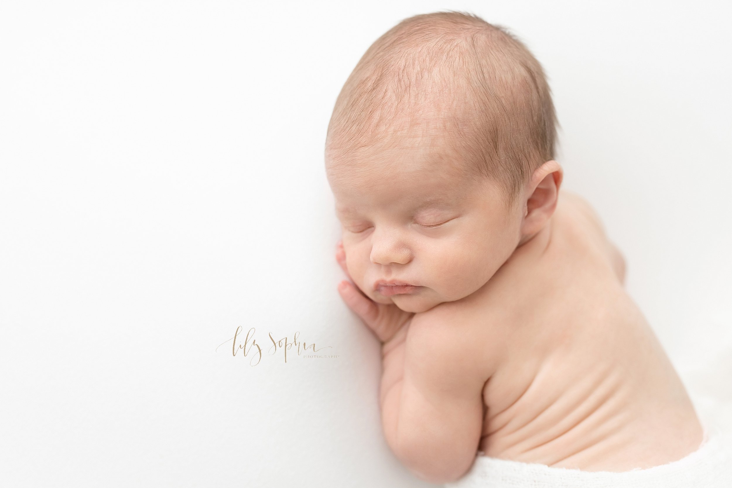  Newborn picture of an infant boy as he lies on his stomach and shows his rolls on his back taken in natural light in a studio near Buckhead in Atlanta. 