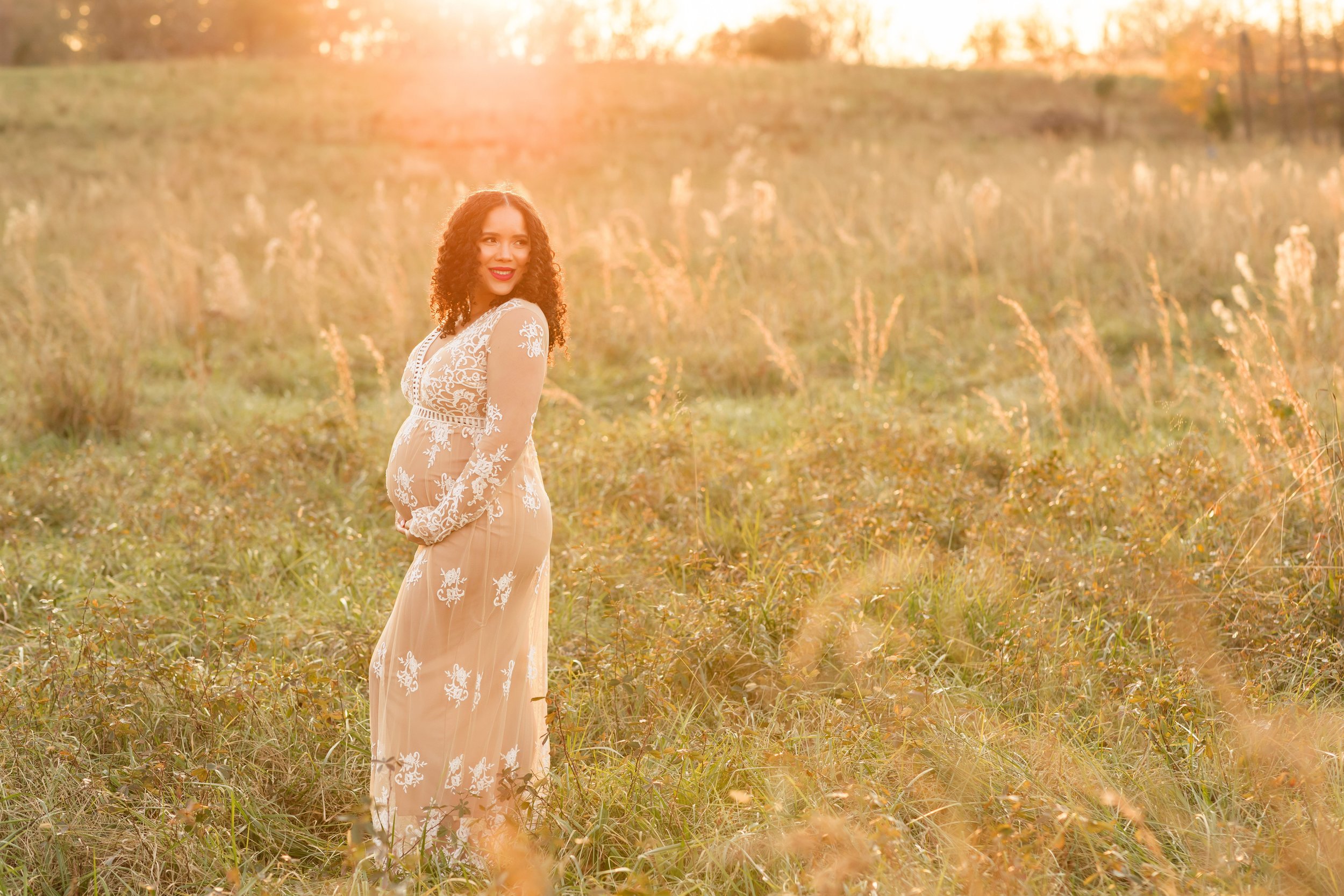  Maternity photo of a pregnant woman as she looks over her left shoulder while standing in a field at sunset near Atlanta, Georgia. 