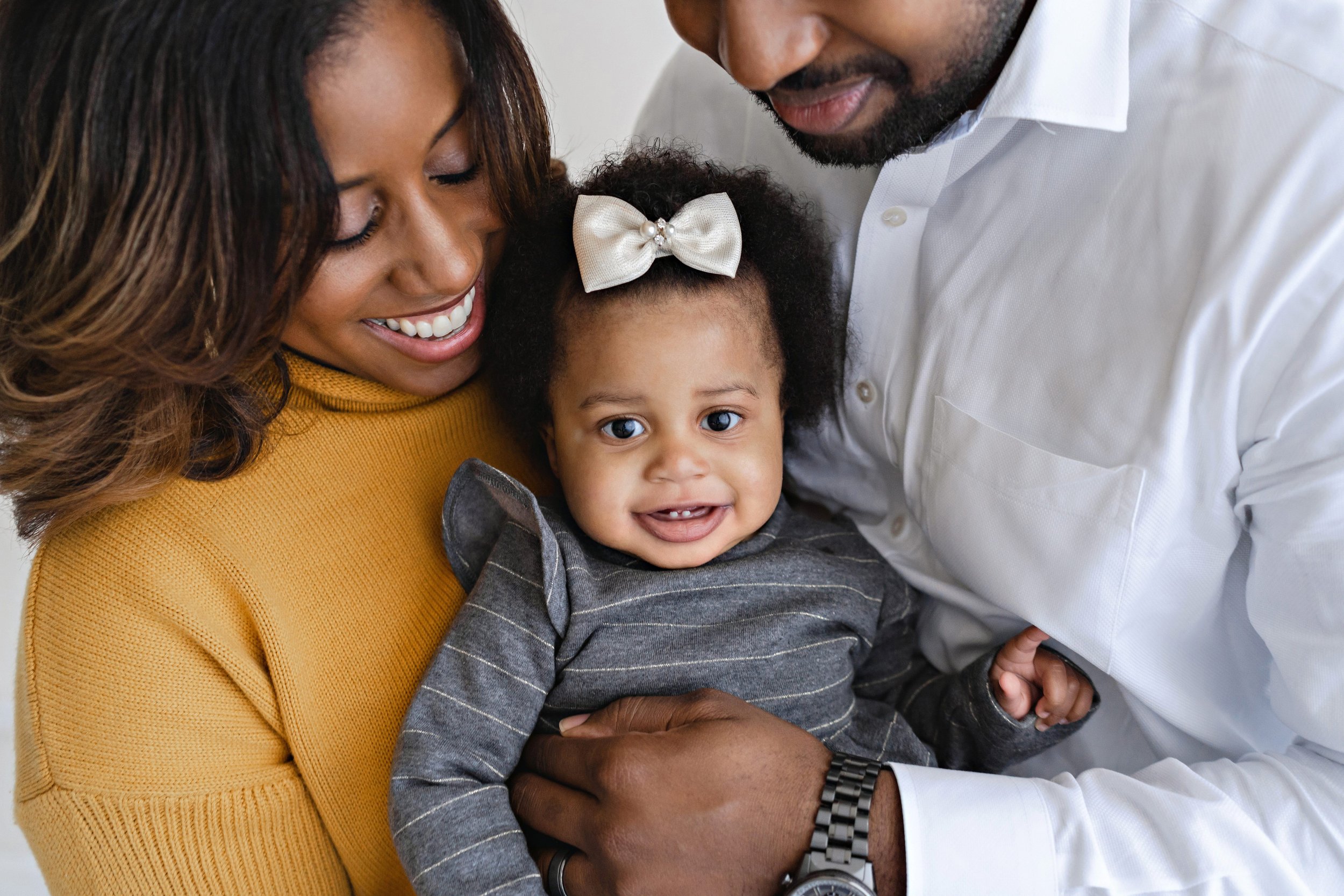  African-American family celebrate a milestone with their one year old daughter with a photo of mom and dad holding their daughter in front of them in a studio in Poncey Market in Atlanta using natural light. 
