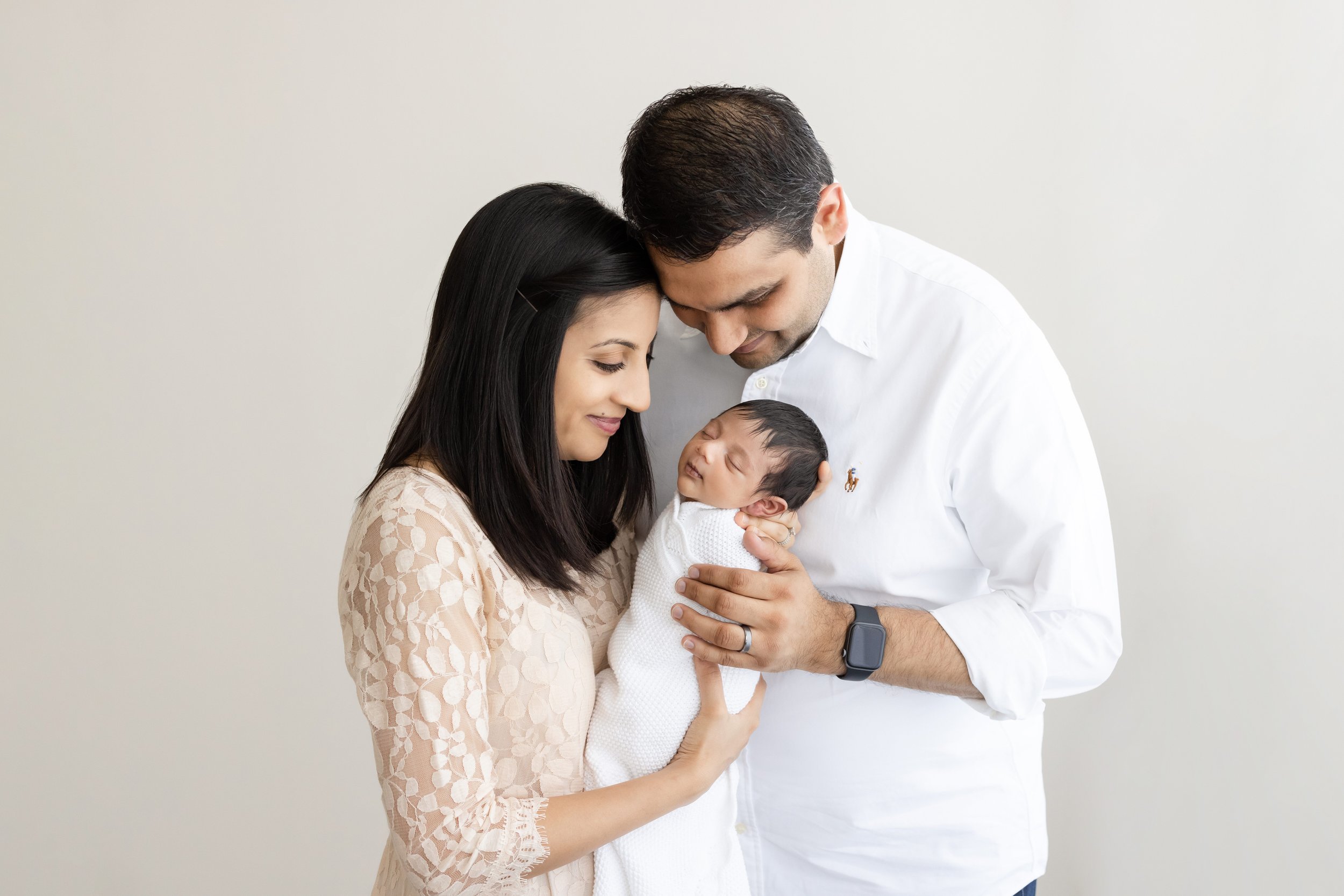  A mother holds her newborn son with his head in her hand and she and her husband admire him as they stand in a photography studio using natural light near Roswell in Atlanta. 