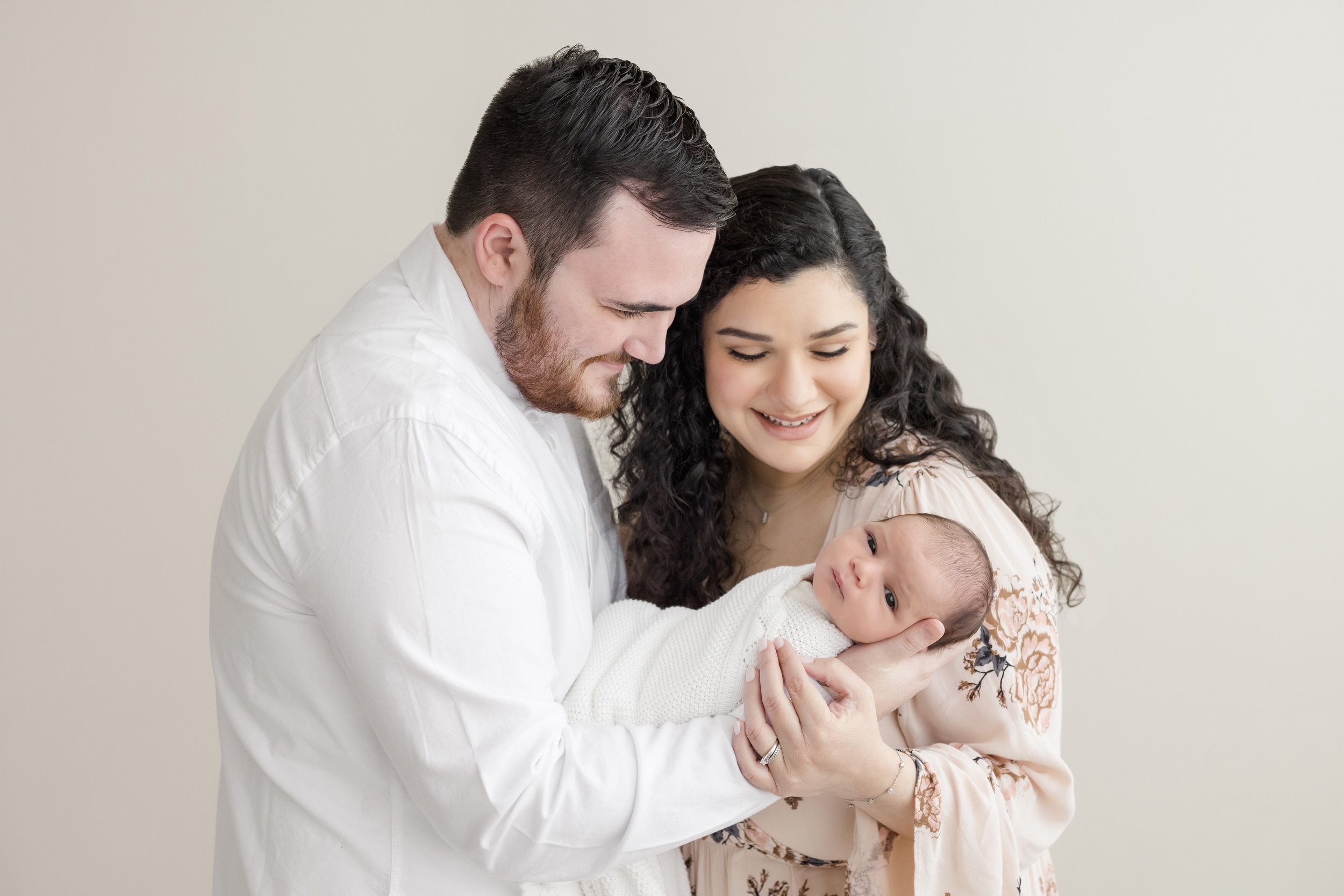  A father holds his wide awake newborn daughter on his arm as his wife stands to his left side and the two of them admire her.  The photo was taken in a natural light studio near Buckhead in Atlanta, Georgia. 