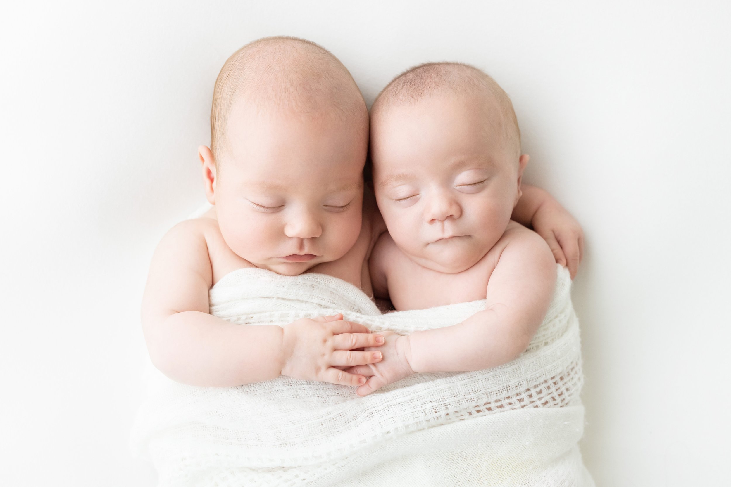  A portrait of sleeping newborn twins wrapped in a single blanket with one of the boys wrapping his arm around his brother’s shoulder as they both put their hands together in front of them taken using natural light near Midtown in Atlanta in Lily Sop