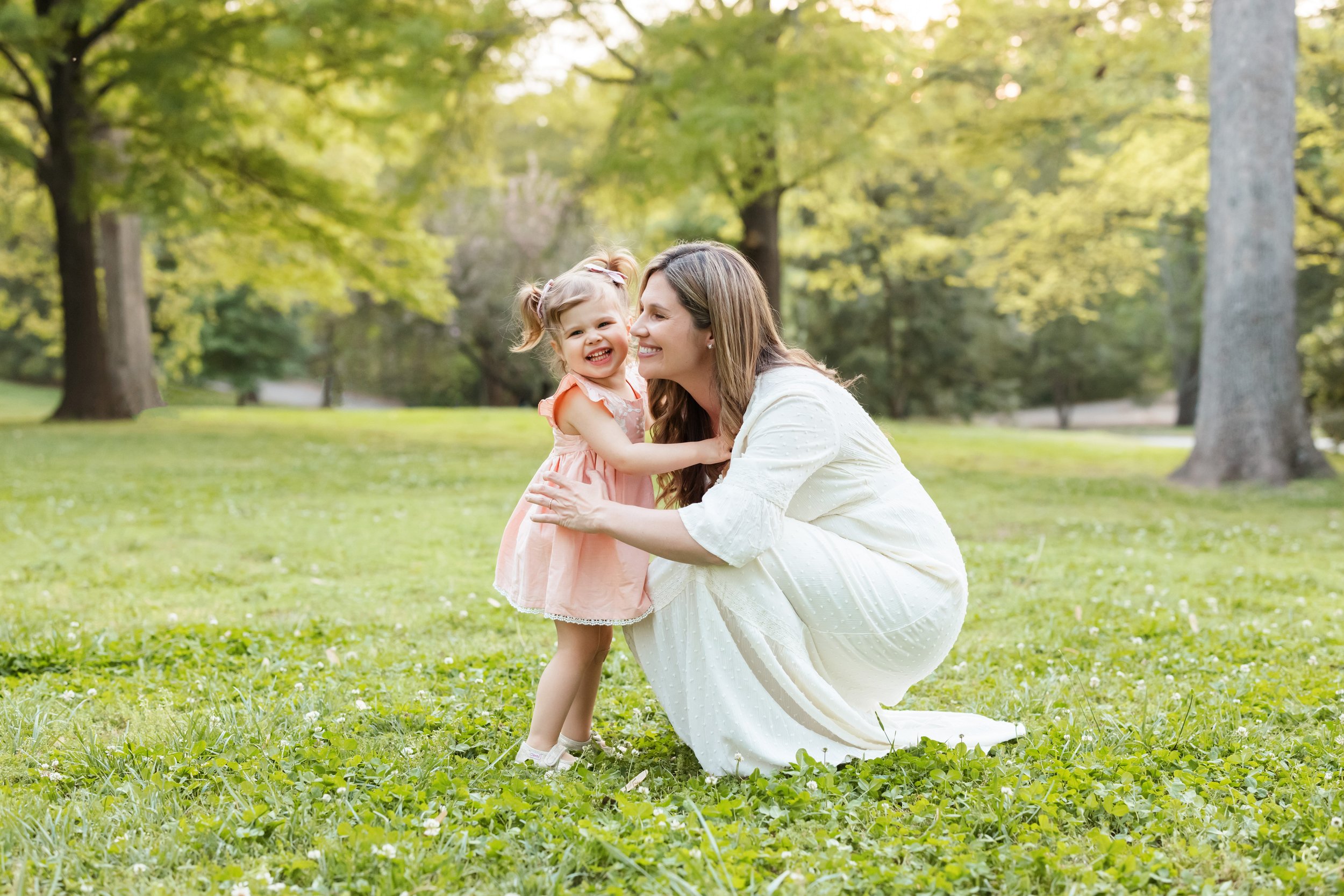  Mother and daughter photo of a mom squatting next to her daughter as she holds her daughter around her waist and talks to her taken at sunset in the spring in a park near Atlanta. 