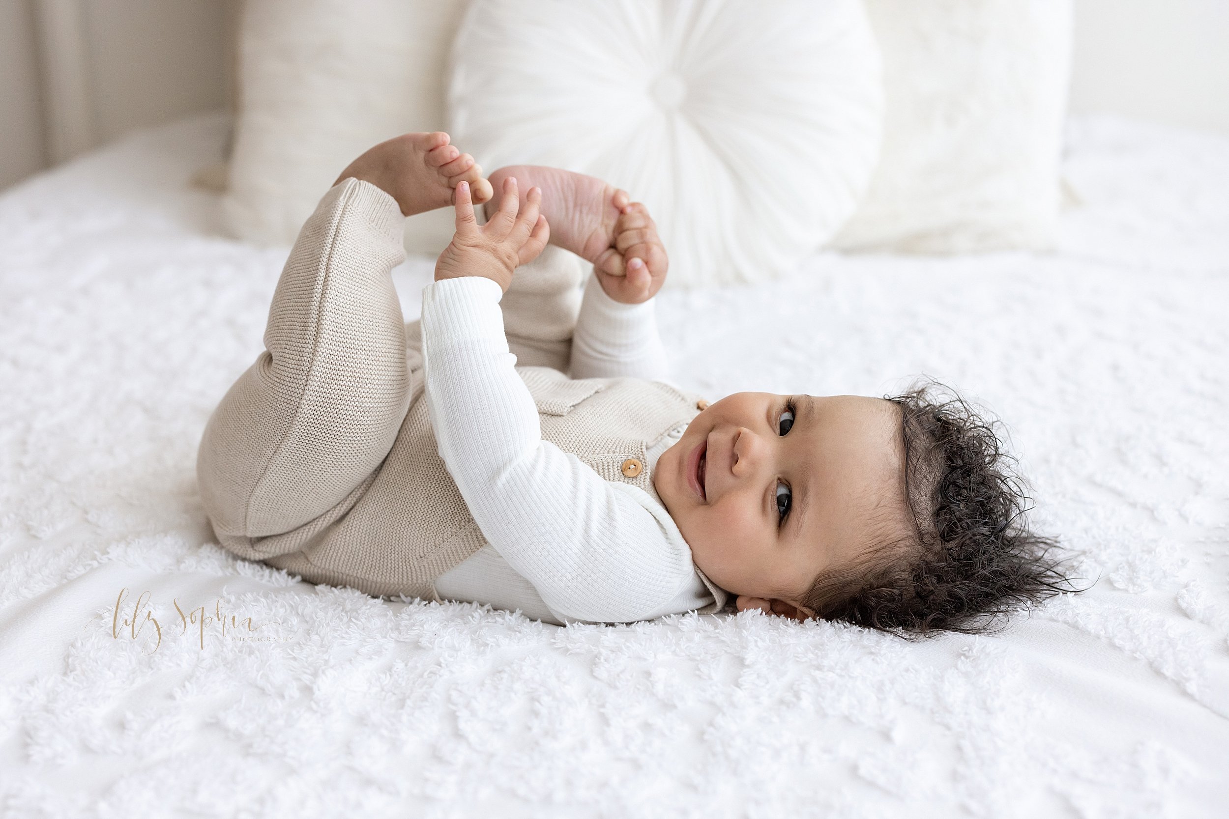  Milestone photograph of a seven month old lying on his back on a bed as he plays with his toes taken in a studio near Old Fourth Ward in Atlanta, Georgia that uses natural lighting. 