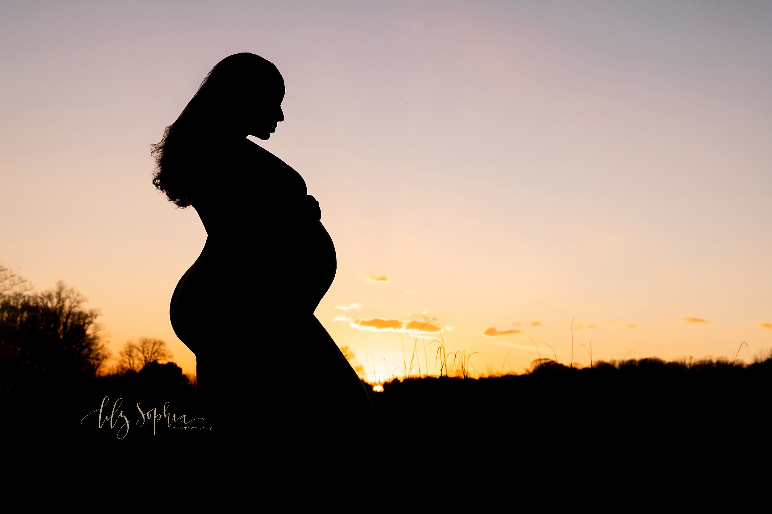  Maternity silhouette of a pregnant mother as she stands at the top of a hill contemplating the birth of her child as the sun sets behind her taken in a field near Atlanta. 