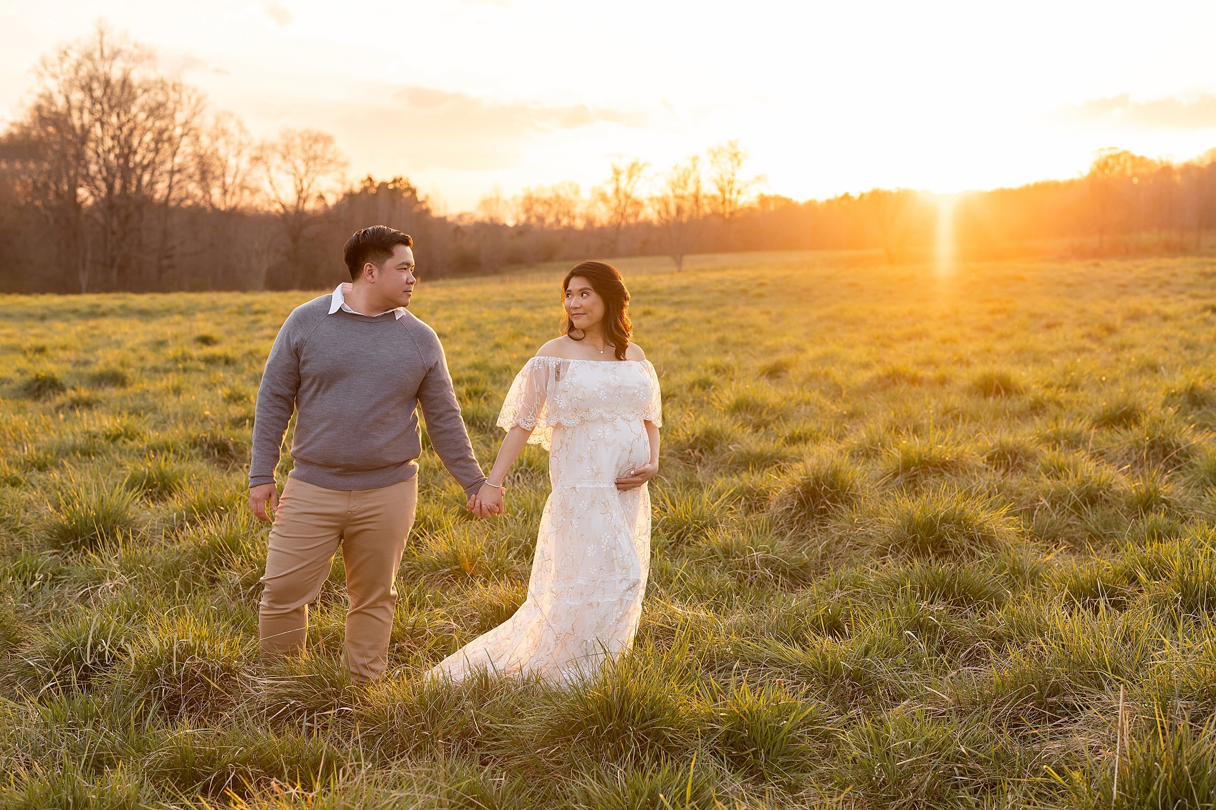  Maternity photo session of a couple standing hand in hand looking at one another in a field near Atlanta at sunset. 