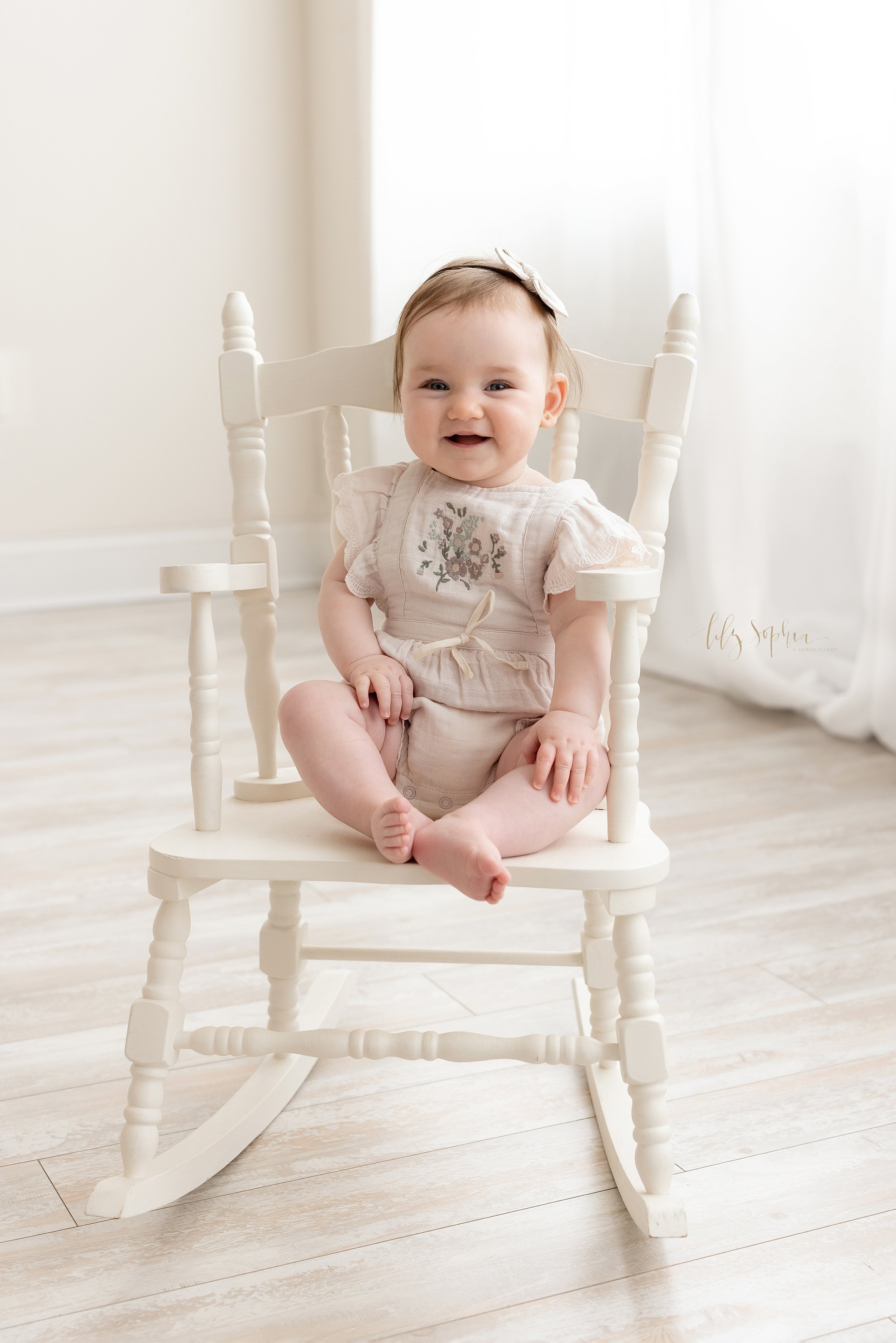  Milestone portrait of a six month old baby girl as she sits in a white rocking chair in front of a window streaming natural light in a studio near Smyrna in Atlanta. 