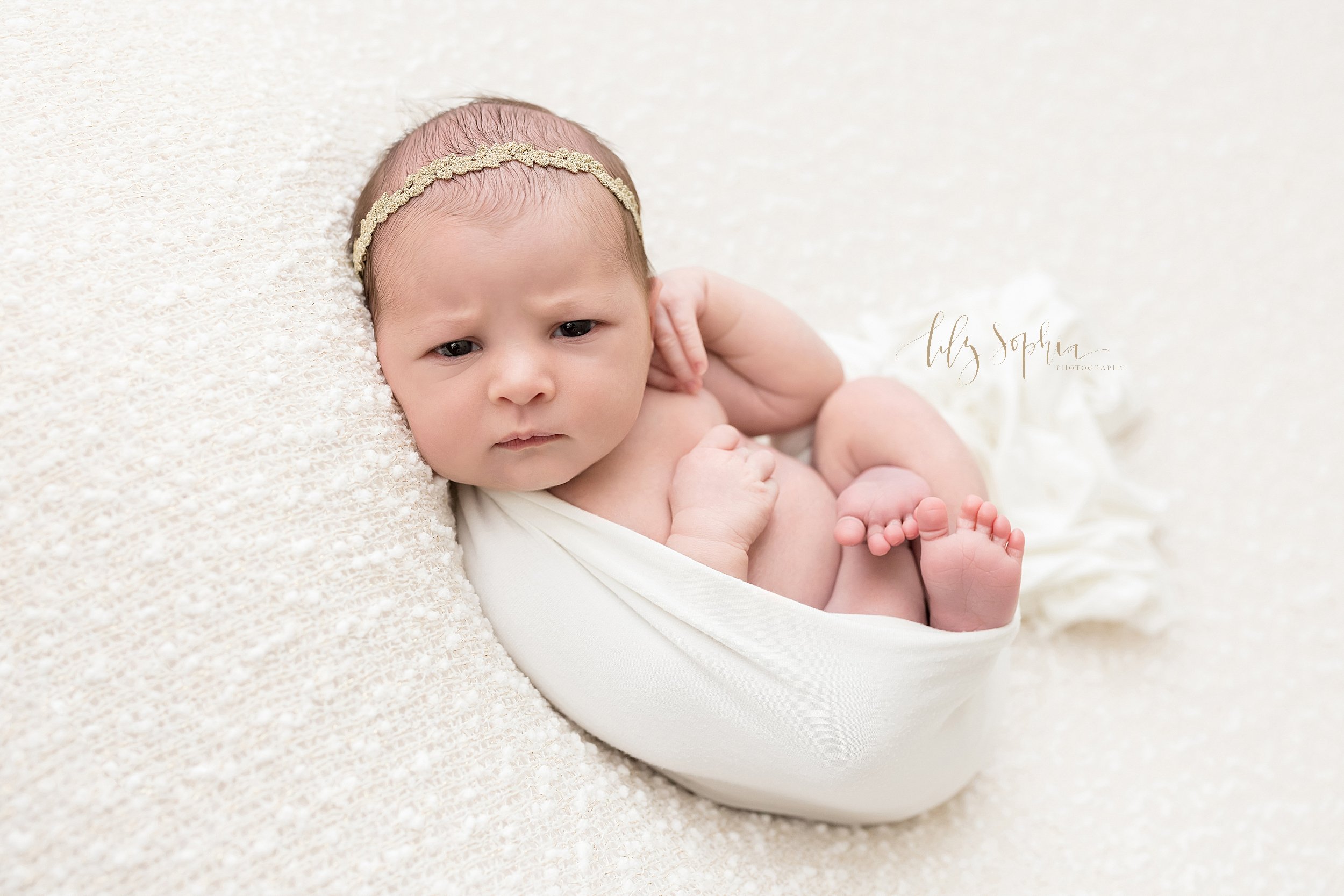  Newborn photo session of an awake infant girl as she lies on her back cradled in a stretchy swaddle taken in a natural light studio near Brookhaven in Atlanta, Georgia. 