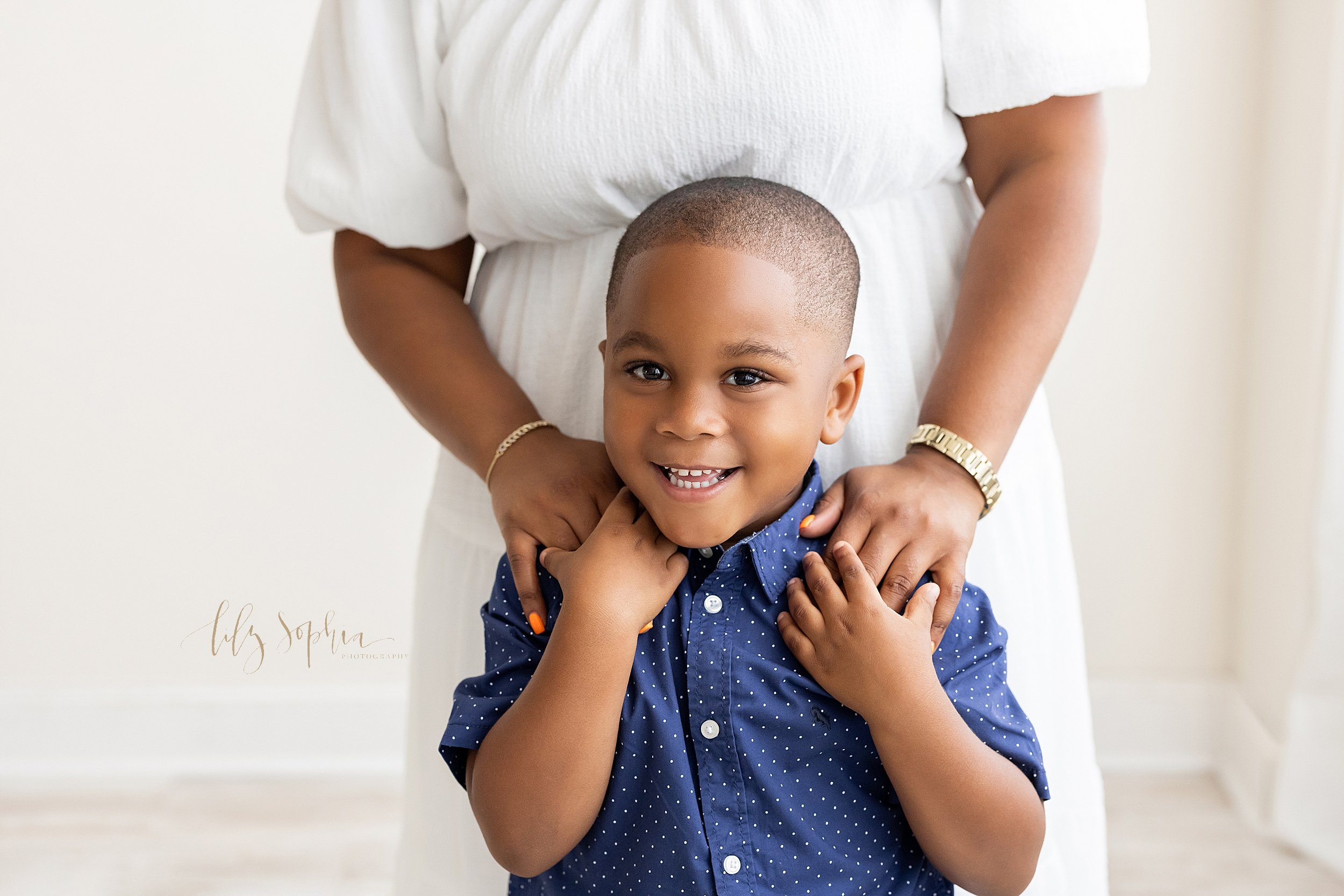 Milestone photo of an African-American five year old boy as he stands in front of his mother and holds her hands that she has placed on his shoulders taken in a natural light studio near Oakhurst in Atlanta, Georgia. 