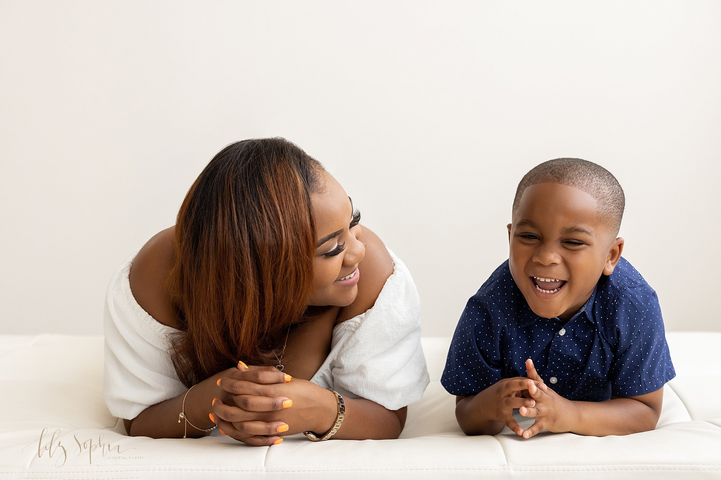  Family portrait of an African-American mother and her five year old son lying across a tufted ottoman as mom talks to her son and he laughs taken using natural light in a studio near Brookhaven in Atlanta. 